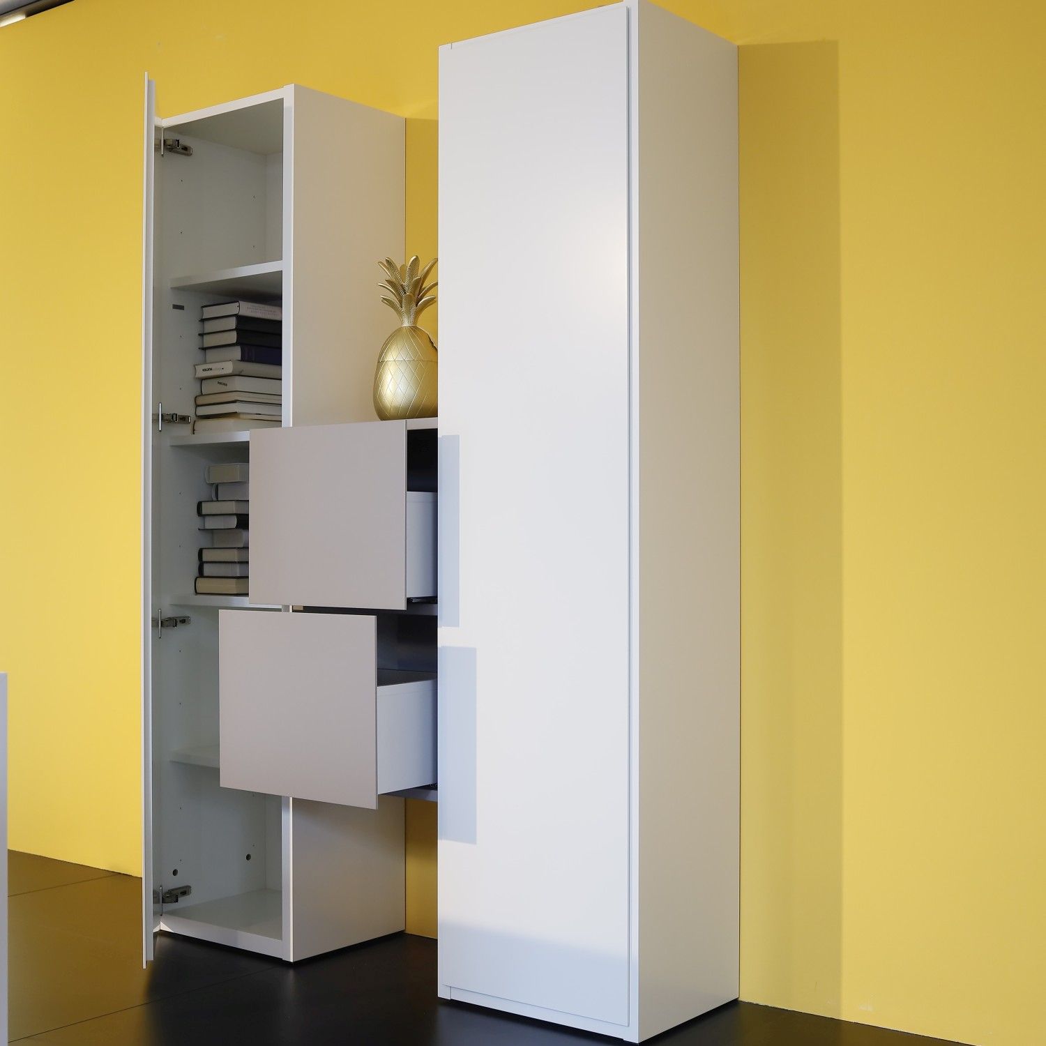 Regalsystem Studimo in Lack matt kristallweiß und taupe im Milieubild vor gelber Wand, linke Türe und Schubladen geöffnet.