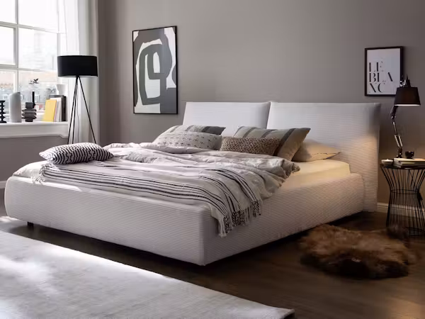 Schlafzimmer mit weißem Polsterbett, Wolldecke und Wandbildern