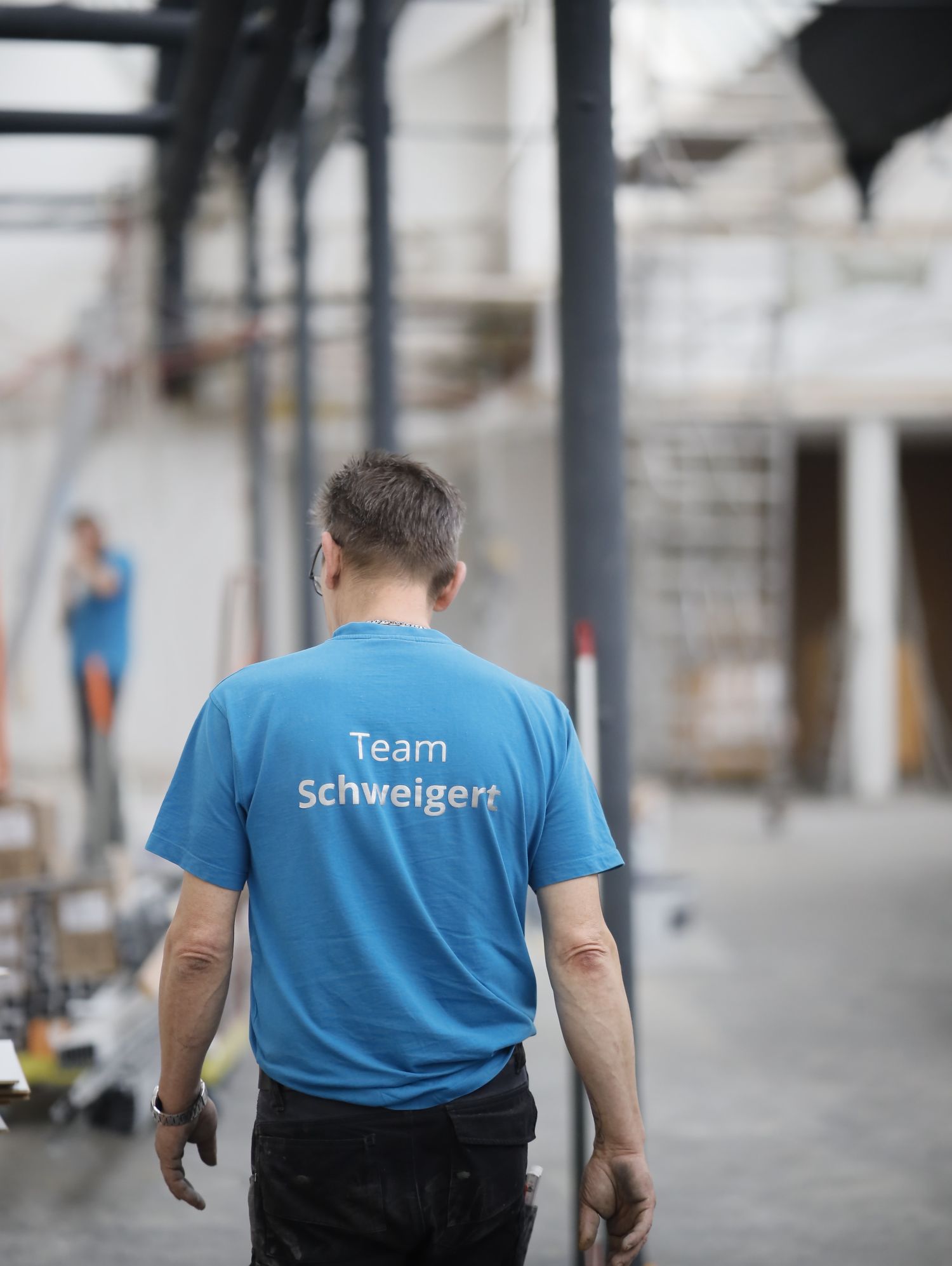 Mitarbeiter im blauen Team-Schweigert-Shirt von hinten in einem Raum im Umbau