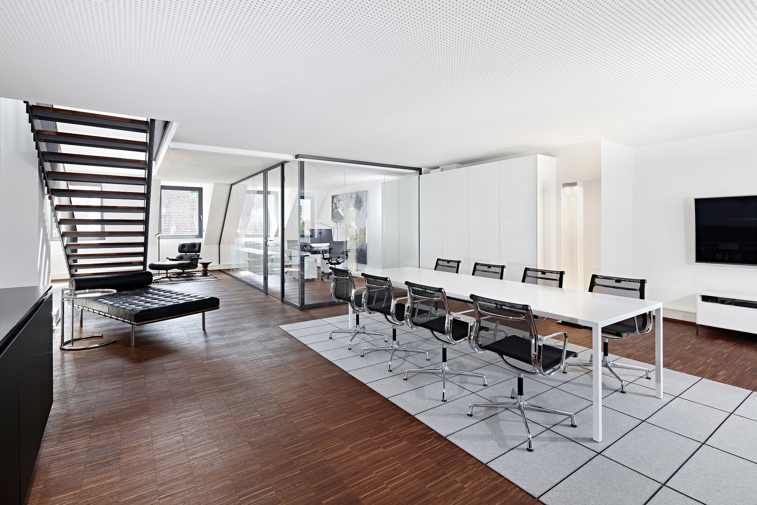 Heller Büro- und Besprechungsraum mit langem Tisch, Holzboden und Treppe