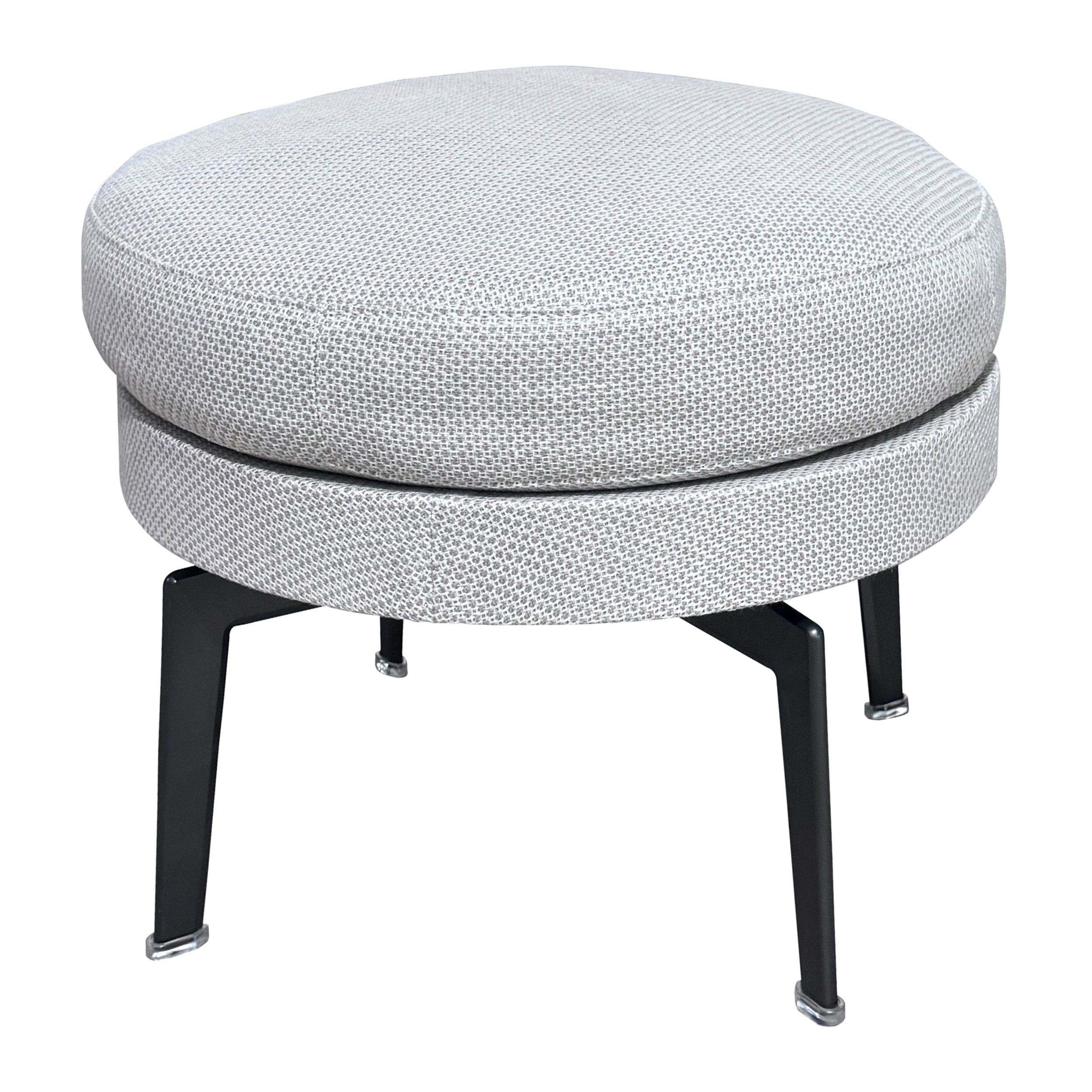 Das Bild zeigt einen runden Hocker mit hellem Stoffbezug und dunklen Metallbeinen, Modell Feel Good von Flexform, in Ansicht von schräg oben vor einem weißen Hintergrund.