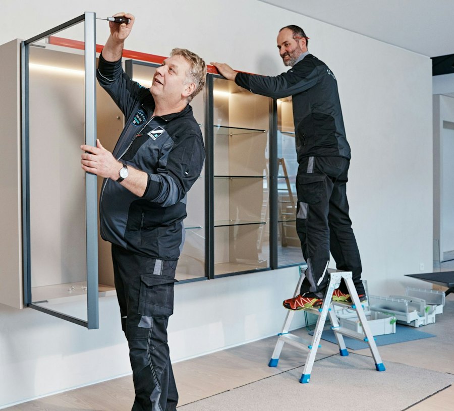 Zwei Schreiner montieren einen Glasschrank mit Metallrahmen