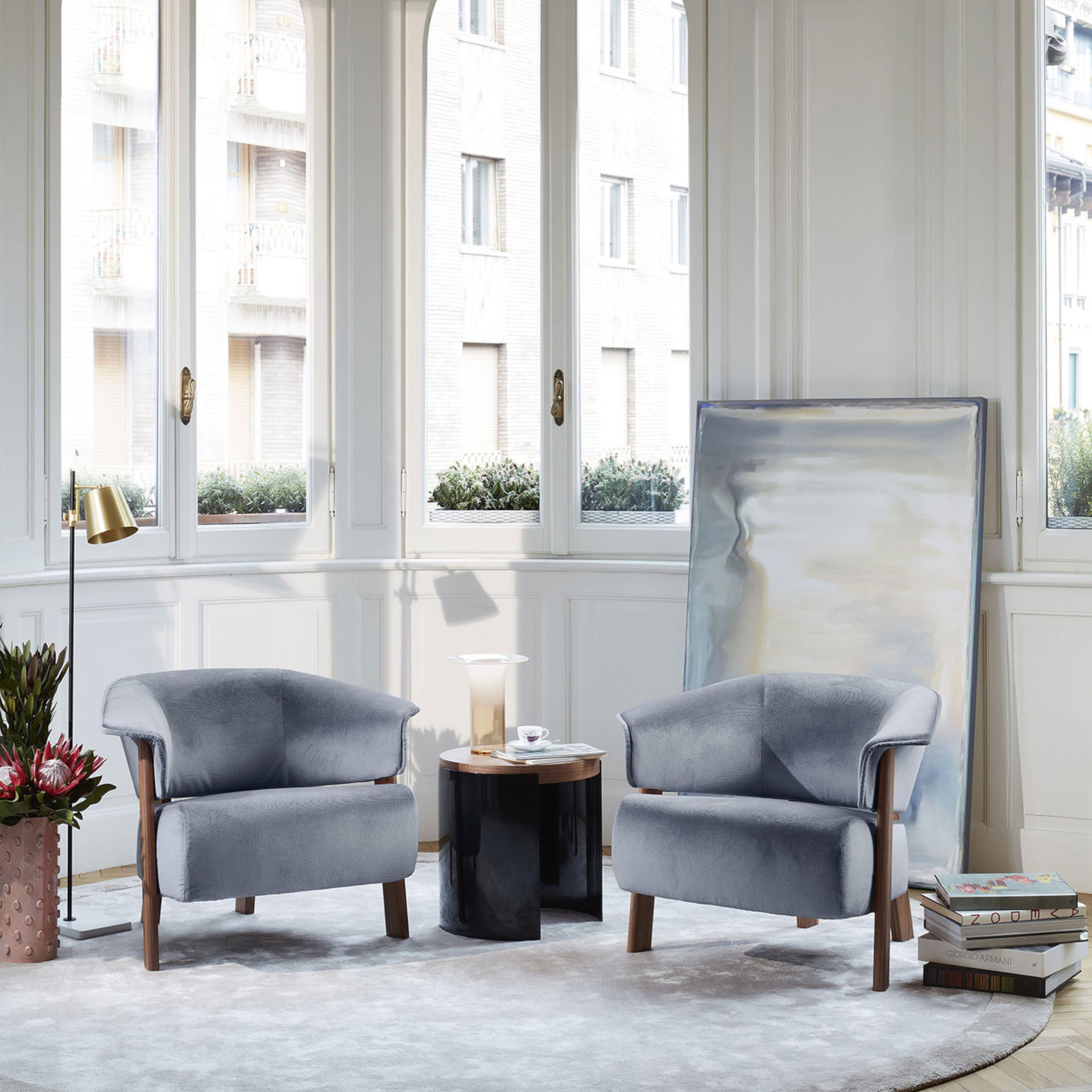 Zwei elegante, hellblau gepolsterte Sessel "Back Wing Armchair "von Cassina und ein Tisch stehen in einem lichtdurchfluteten Raum mit großen Fenstern.