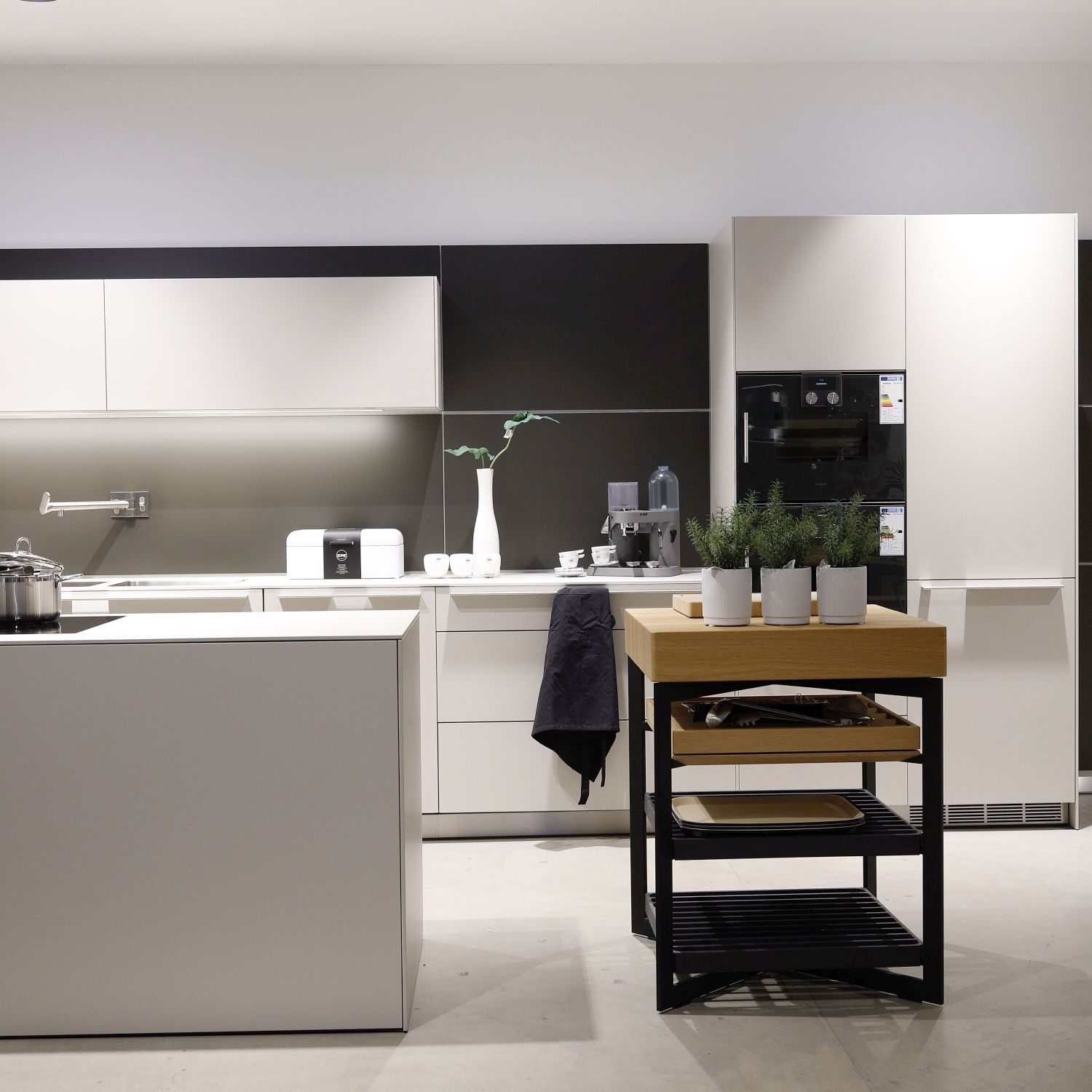 Zu sehen ist ein schwarzes Metallgestell mit Holzarbeitsplatte in einer hellen Designer-Küche, dekoriert mit Töpfen mit Küchenkräutern.