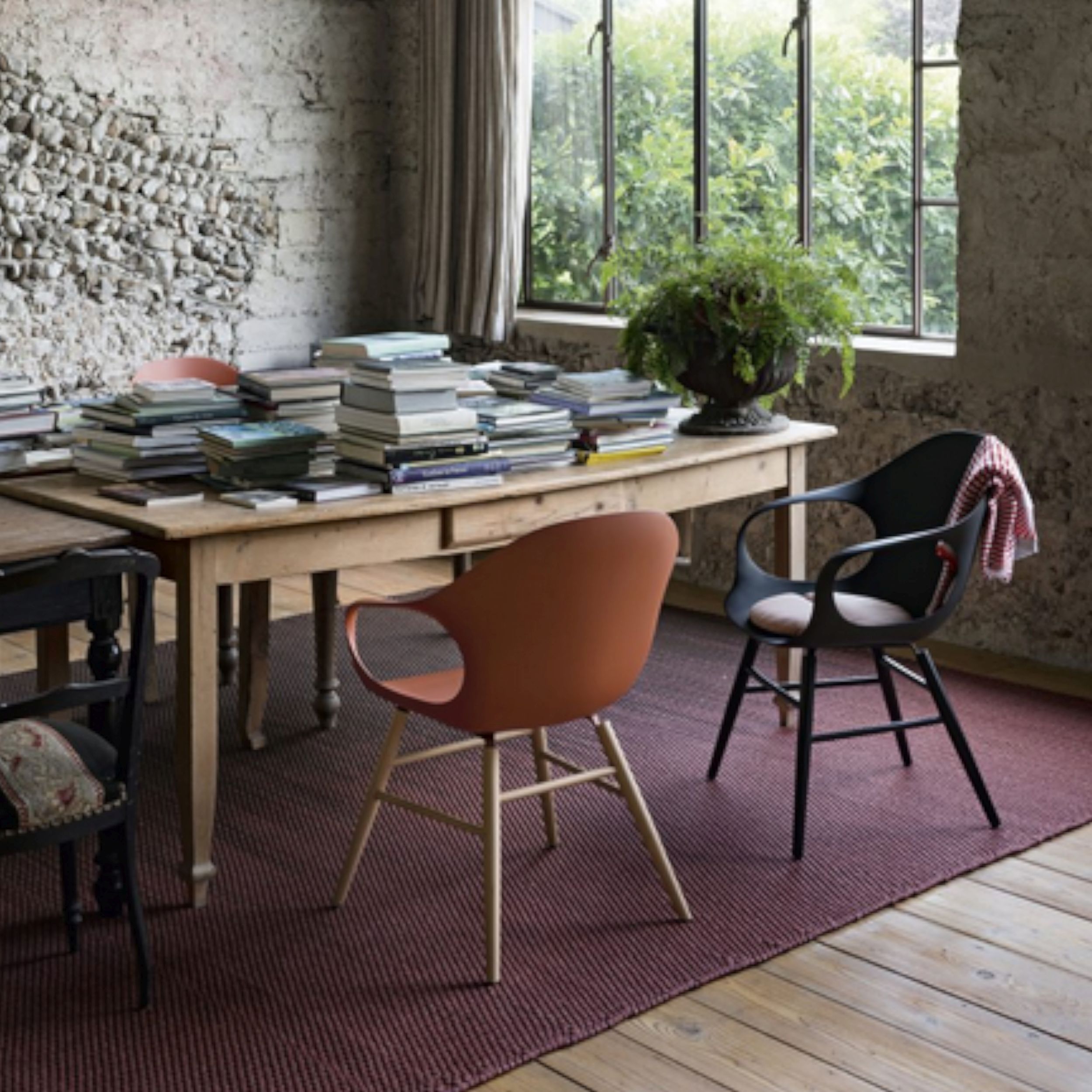 Das Bild zeigt das Stuhlmodell Elephant von Kristalia in einem gemütlichen Esszimmer. Die Stühle stehen vor einem rustikalen Holztisch der mit Bücherstapeln bedeckt ist.