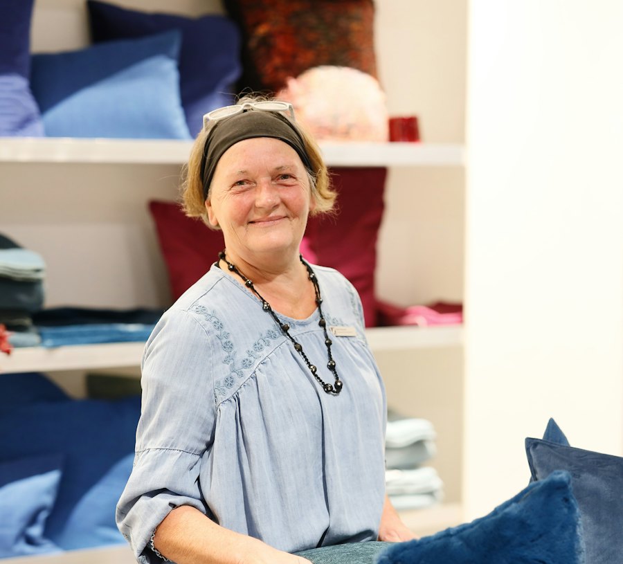 Lächelnde Mitarbeiterin der Boutique vor Kissen und Heimtextilien