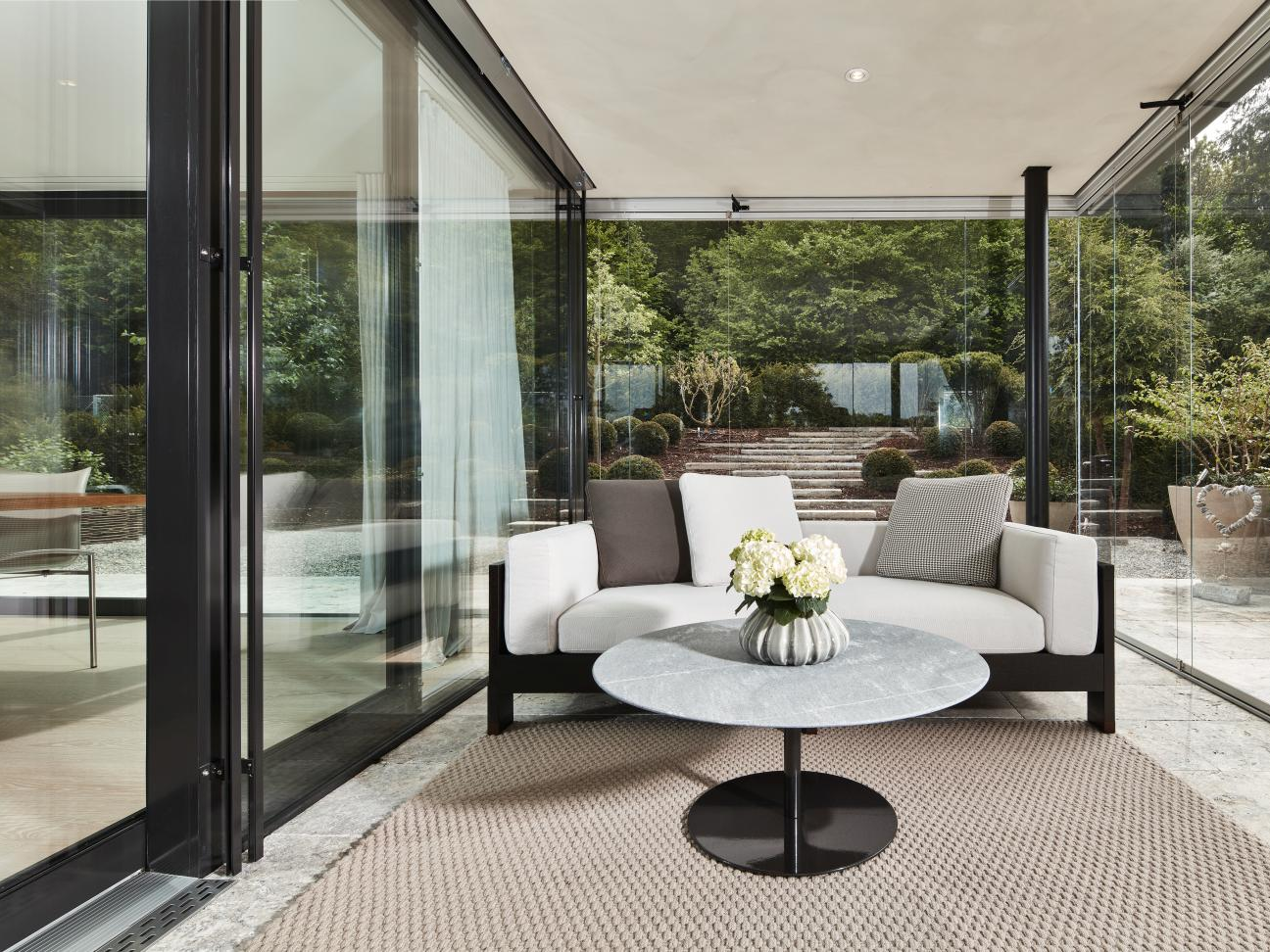 Outdoor-Sofa mit rundem Couchtisch auf einer Terrasse vor Glasfront