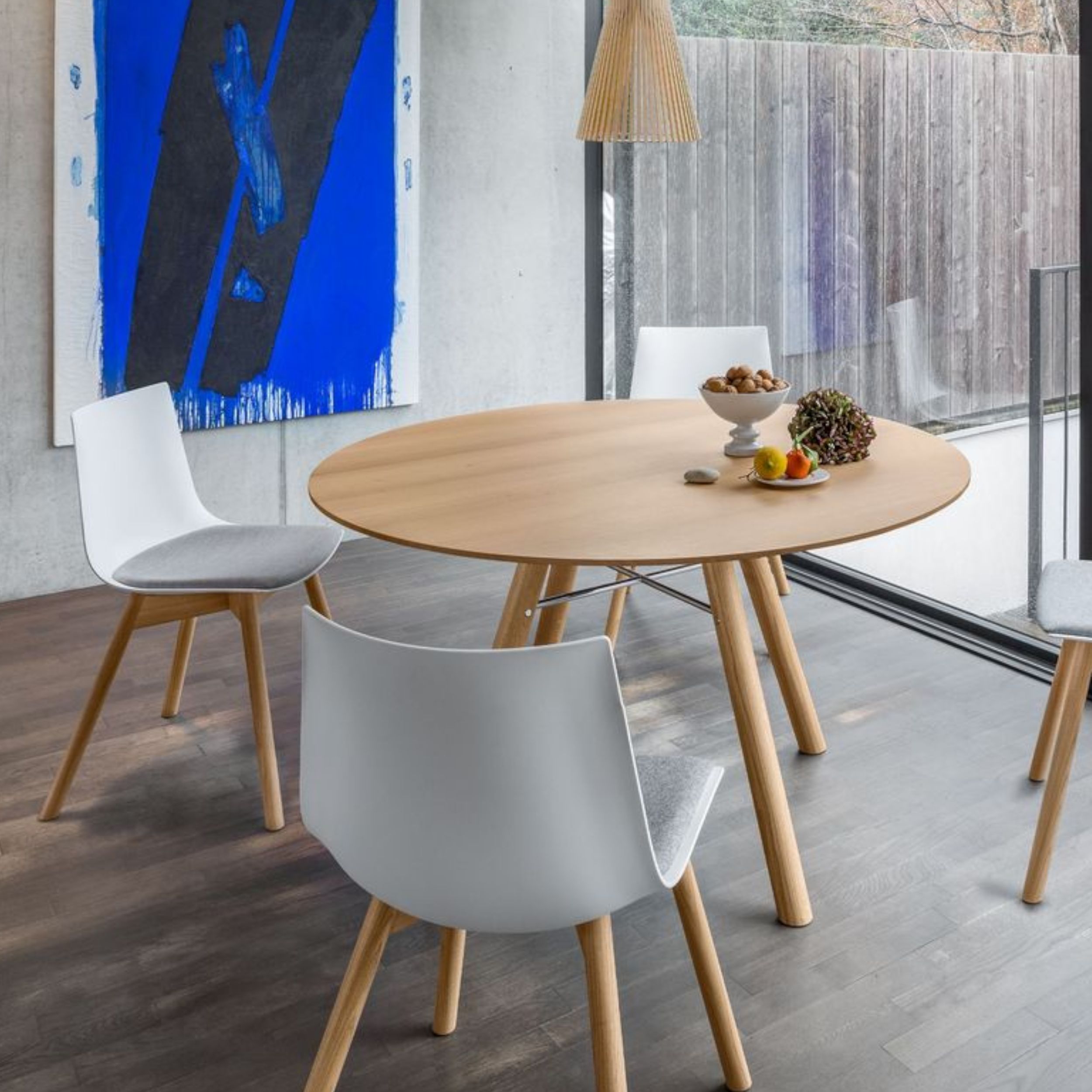 Das Bild zeigt eine moderne Essgruppe im skandinavischen Stil vor einer Betonwand mit einem leuchten blauen Gemälde.