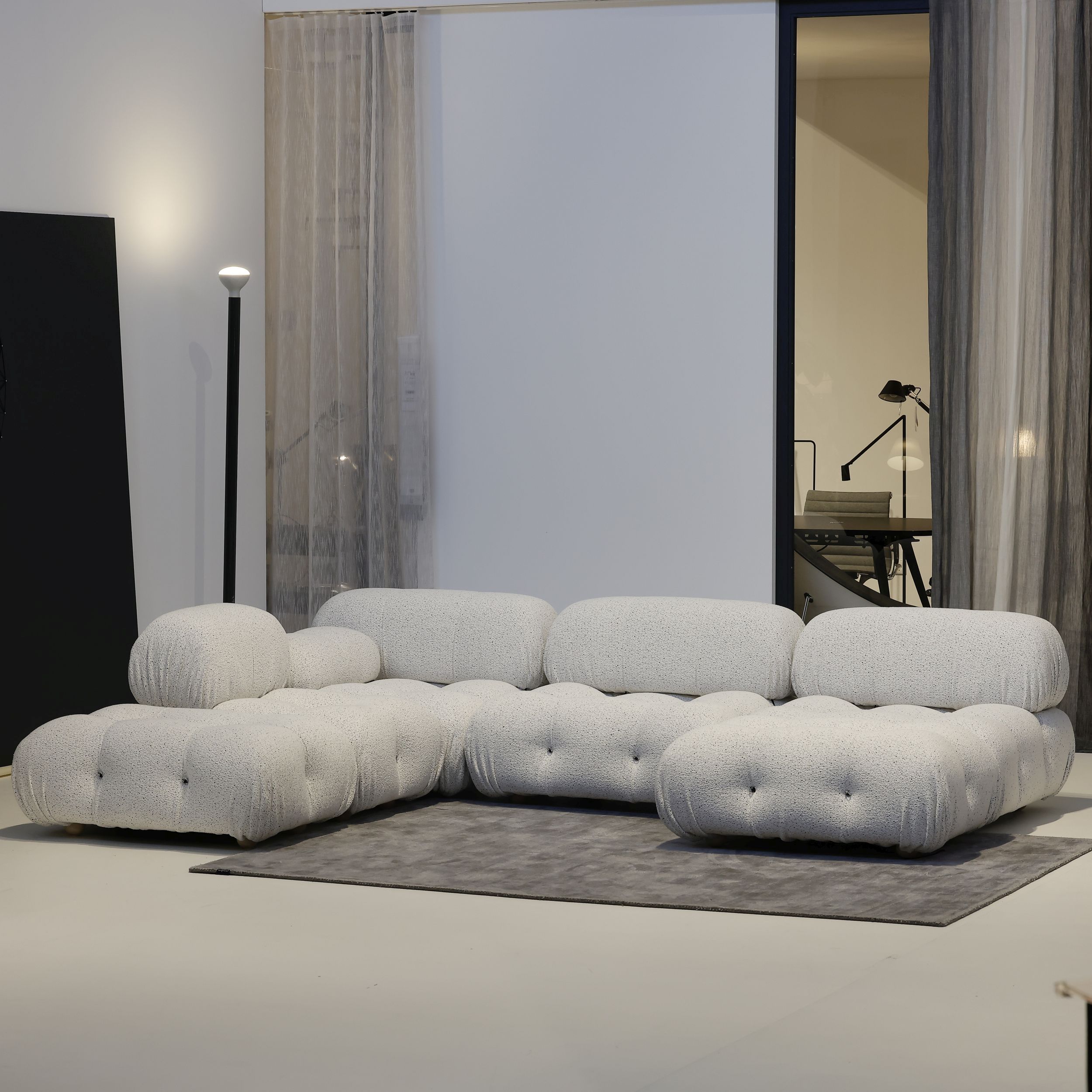 Auf dem Bild sieht man das modulare Sofamodell Camaleonda von B&B Italia vor weißem in einer U-förmigen Zusammenstellung und weißem Stoffbezug vor einer weißen Wand und grauen Vorhängen.