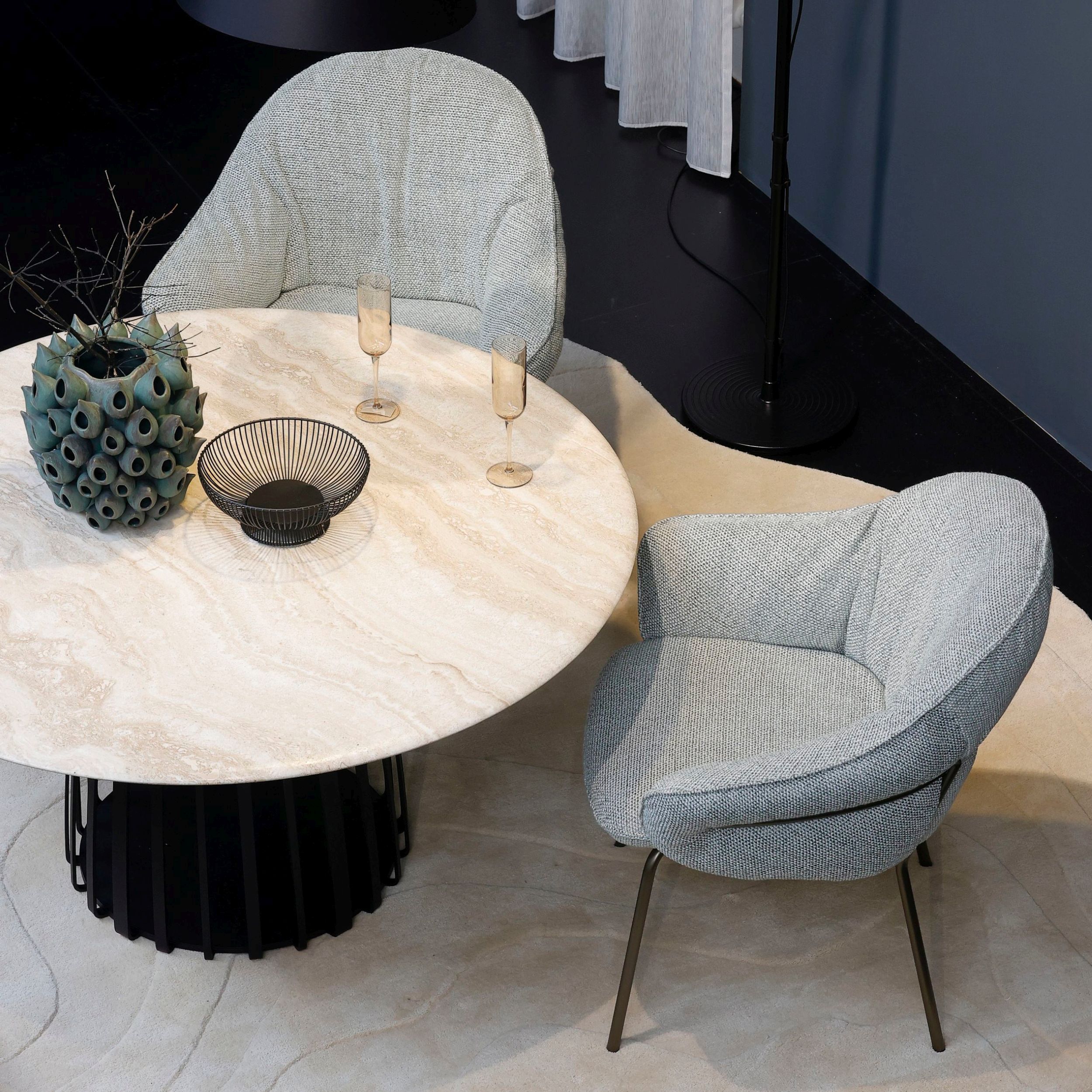 Zu sehen ist eine elegante Essgruppe Low Dining von Freifrau bestehend aus rundem Esstisch Basket  mit heller Steinplatte und hellgrün gepolsterten Stühlen Marie.