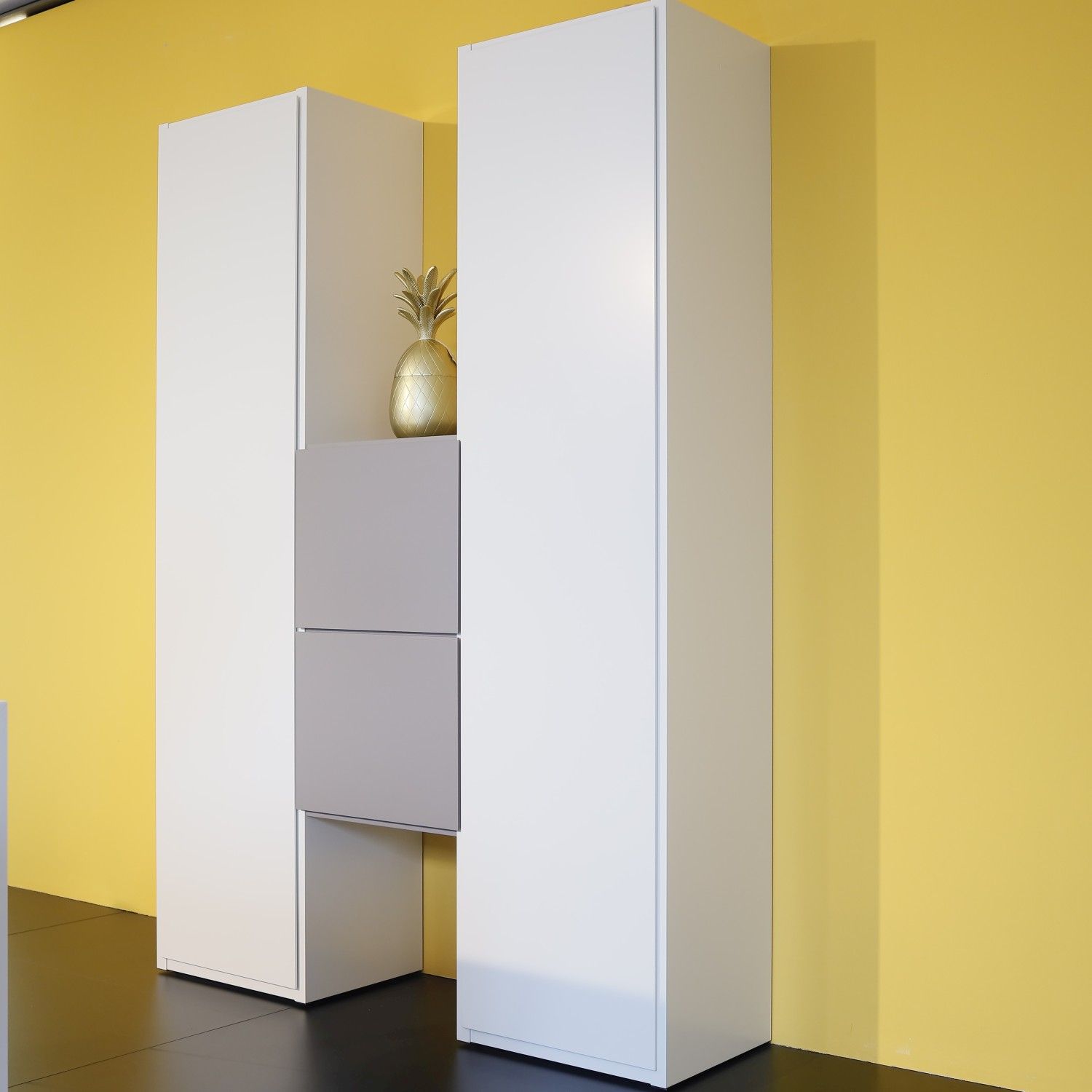 Regalsystem Studimo in Lack matt kristallweiß und taupe im Milieubild vor gelber Wand.