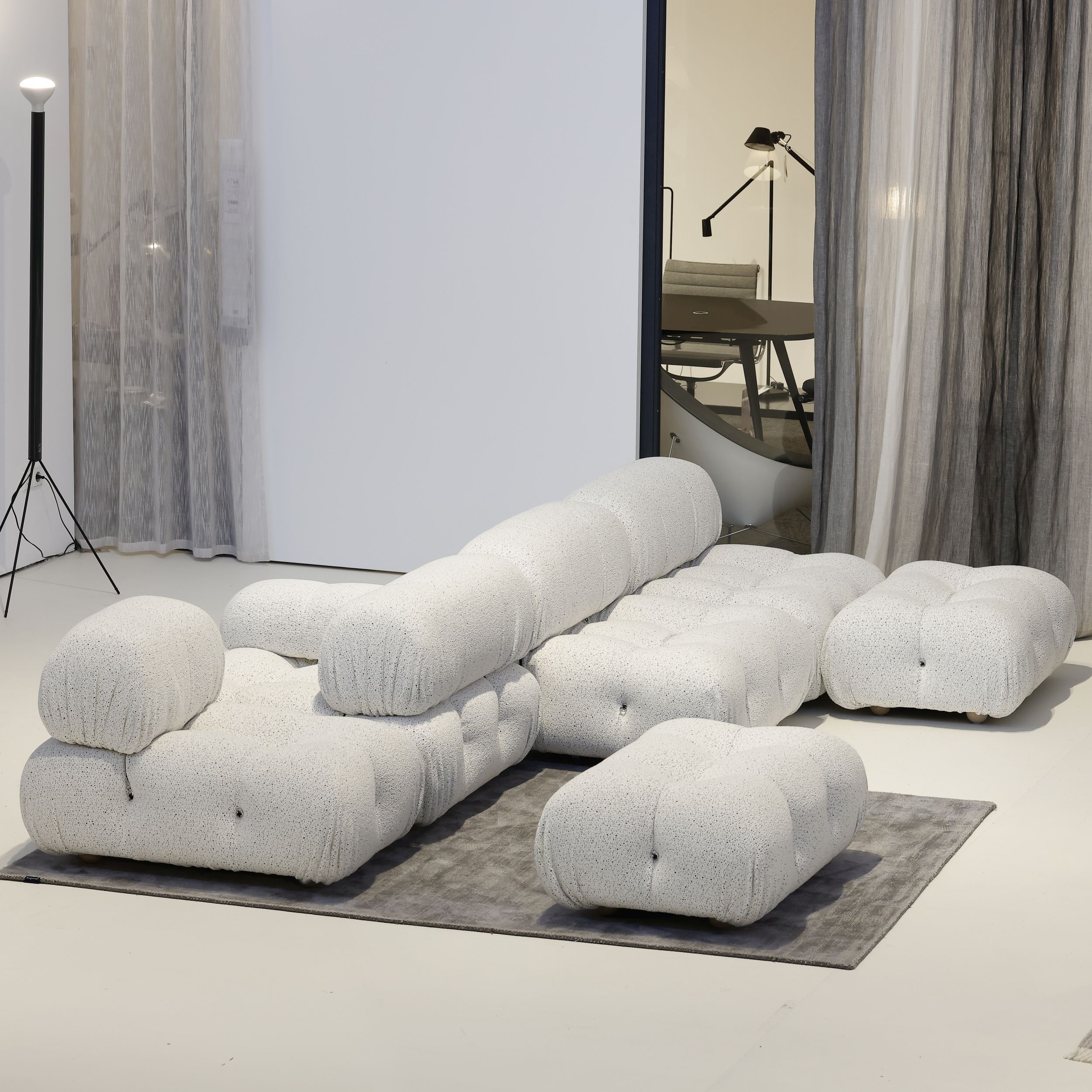 Auf dem Bild sieht man das Sofamodell Camaleonda von B&B Italia in einem modernen Studio. Gezeigt wird das Sofa mit einer Rückenlehne in der Mitte und rechts und links davon angeordneten Sitzflächen; im Vordergrund steht ein einzelner Hocker. Das Sofa ist