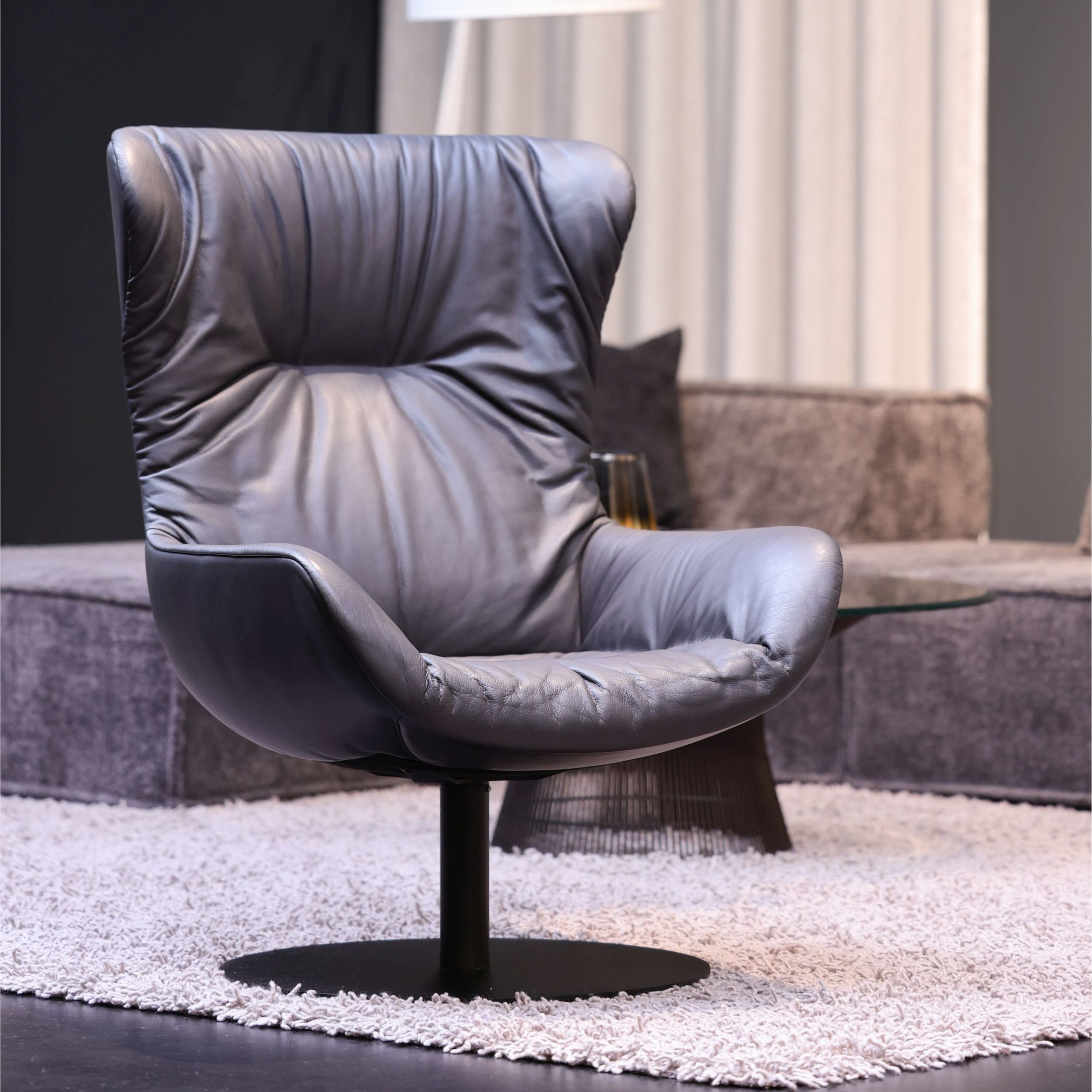 Das Bild zeigt den anthrazitfarbenen Ledersessel Leya Wingback Chair in einem modernen Umfeld auf einem hellen Teppich.