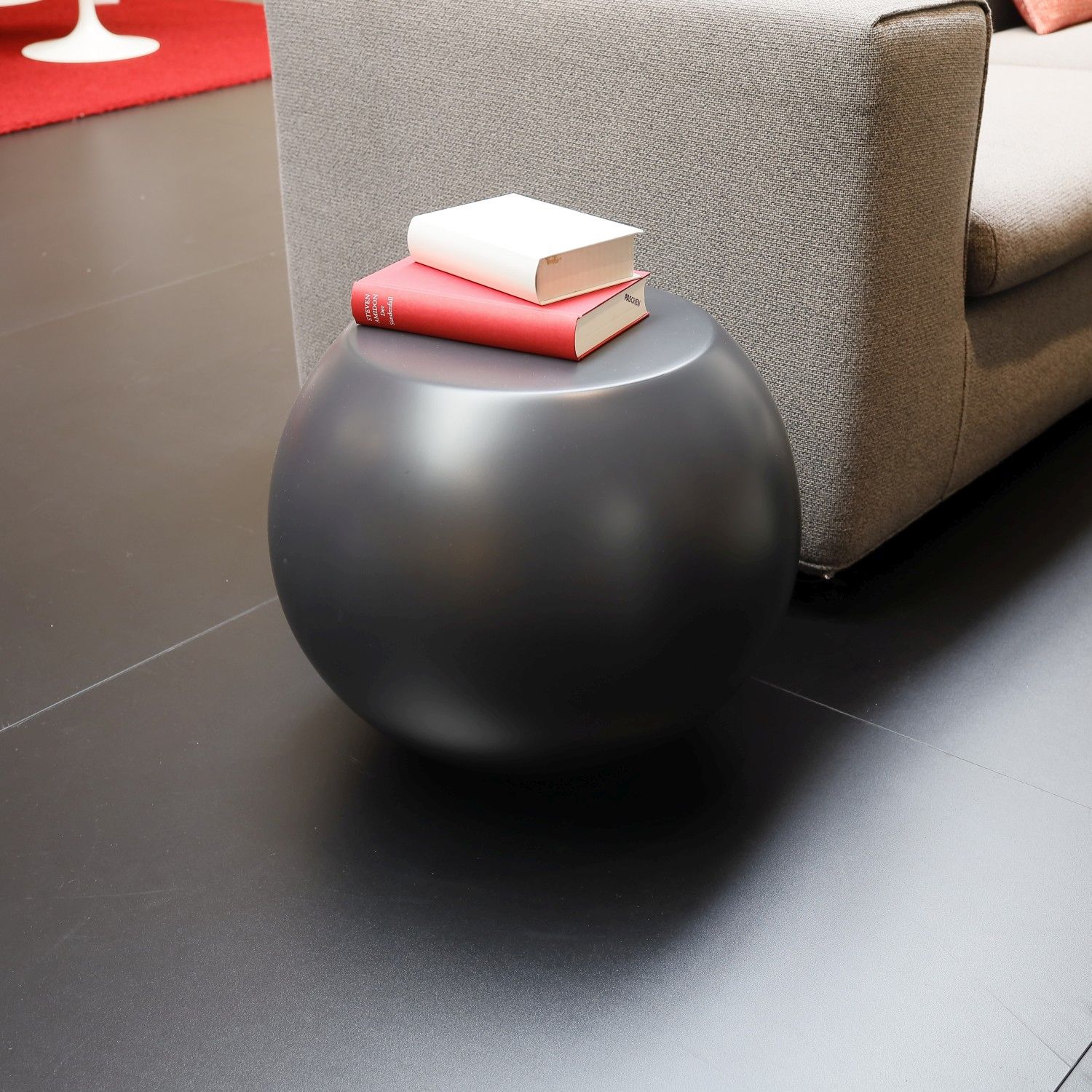 Bunder Beistelltisch Bong von Cappellini in anthrazit neben einem grauen Stoffsofa; auf dem Tisch liegen zwei Bücher.