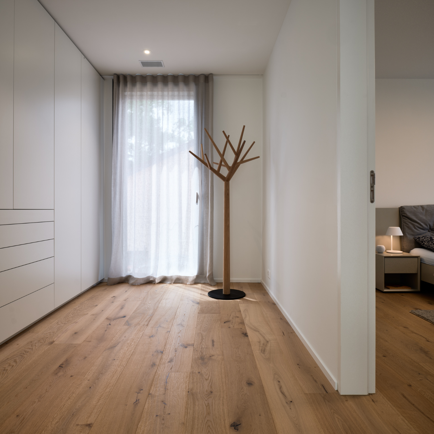 Flur mit weißem Einbauschrank, Garderobenbaum und Eichenboden