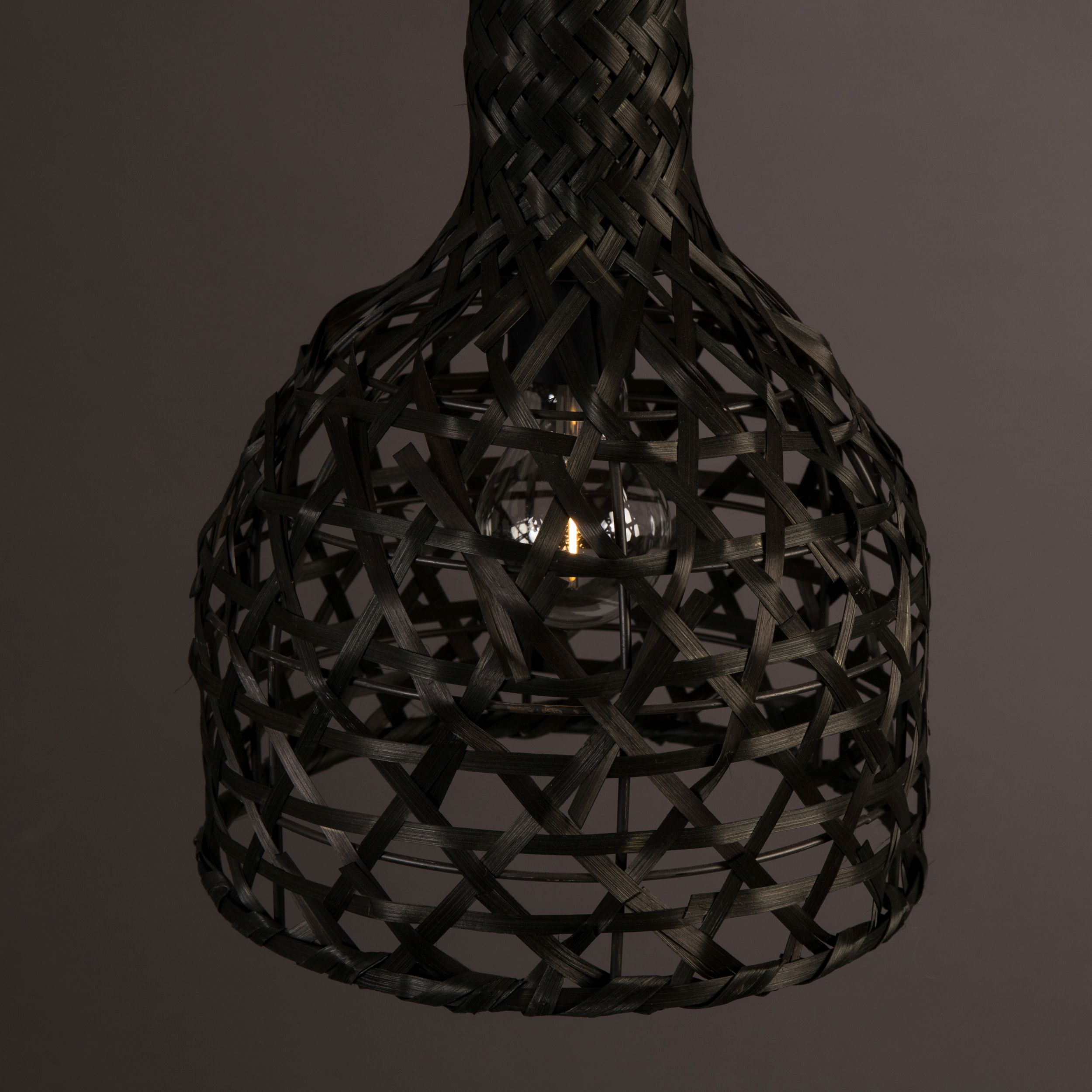 Detailansicht einer schwarzen Boho-Hängelampe mit durchbrochenem Rattan-Geflecht und sichtbarem Leuchtmittel vor dunkelgrauem Hintergrund.
