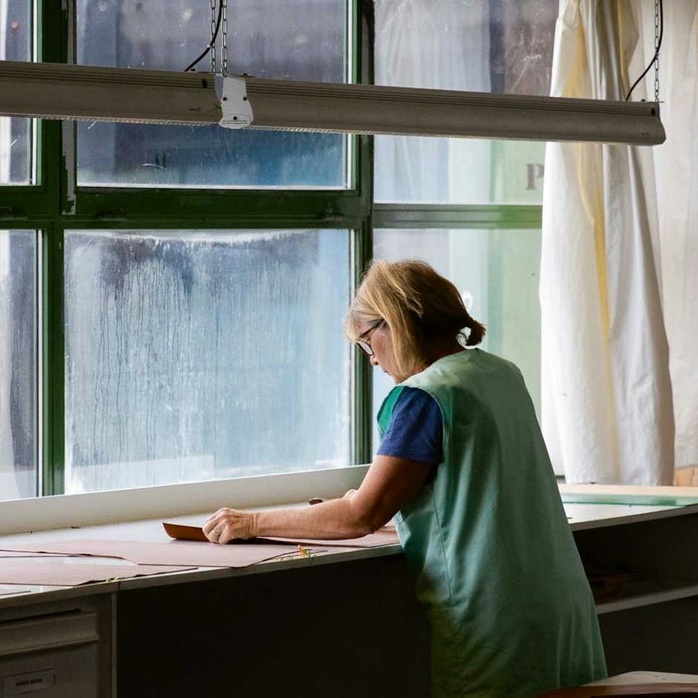Mitarbeiterin der Raumausstattung arbeitet an einem Stoff am Fenster