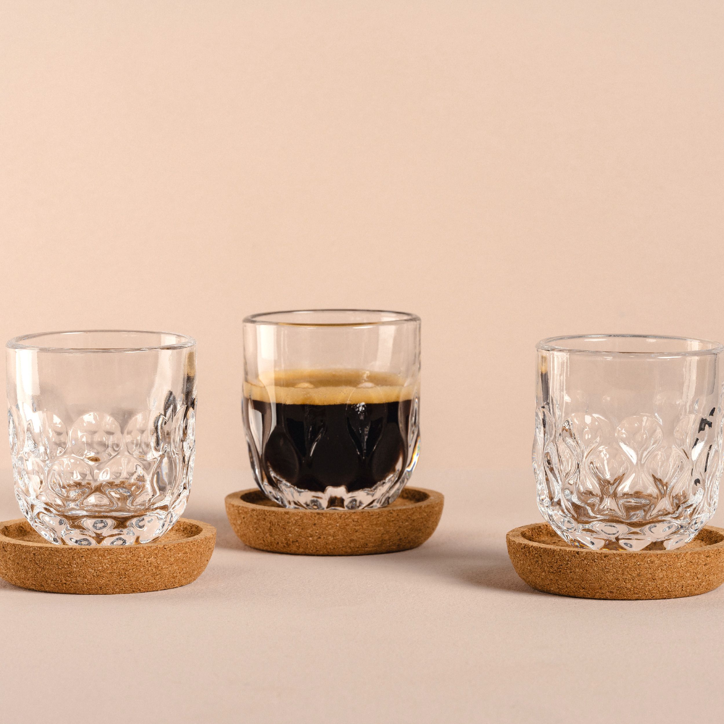 Espressoglas 6 tlg.  klar Gocce von Leonardo
best. aus 3 Gläser mit Korkuntersetzer.
Gläser haben ein elegantes Tropfenrelief.
Das mittlere Glas ist mit Espresso gefüllt und stehen vor einem beigen  Hintergrund. 
