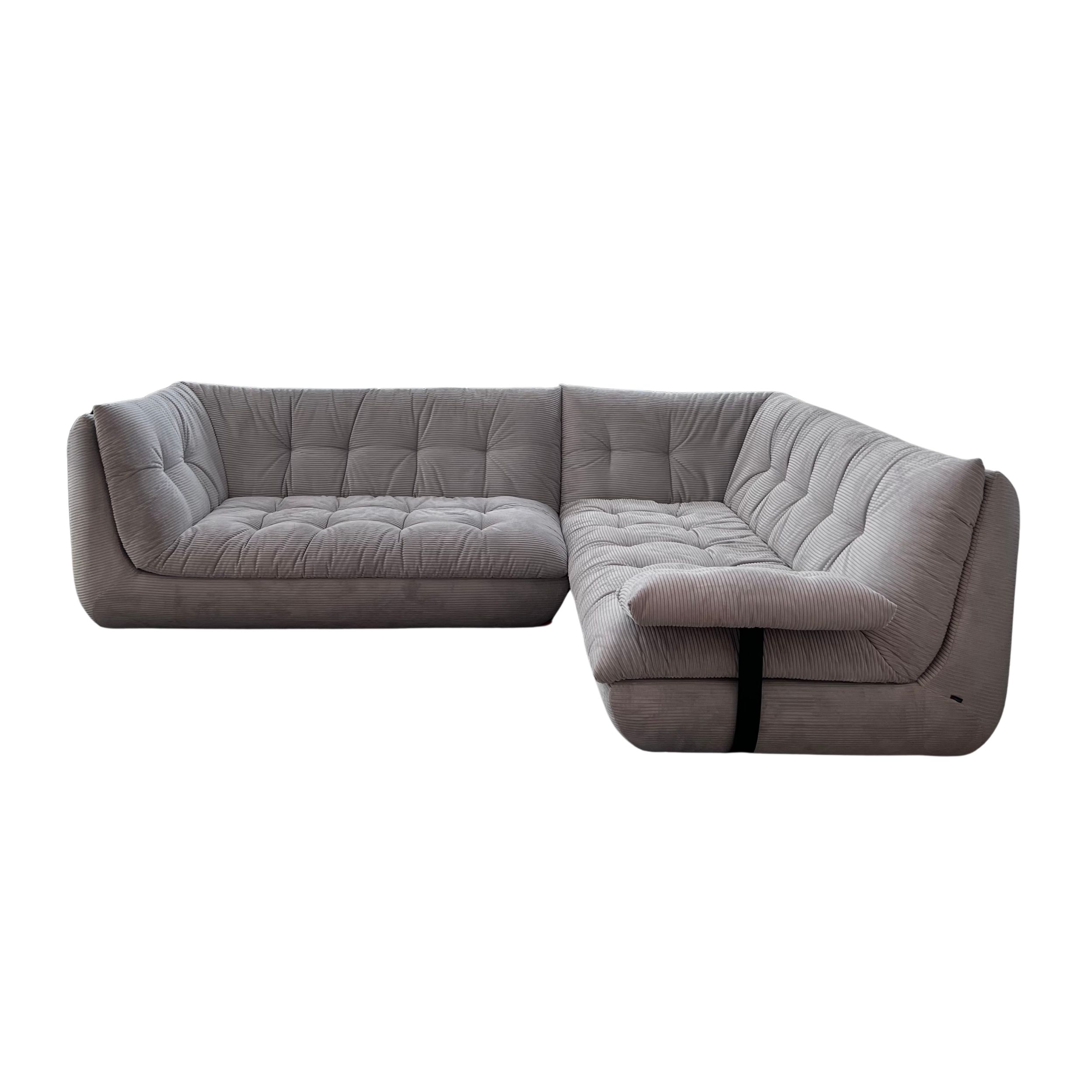 Zu sehen ist ein L-förmiges Sofa in hellem Stoff mit abgesteppter Polsterung, Modell Soulmate von ipDesign, vor einem weißen Hintergrund. 