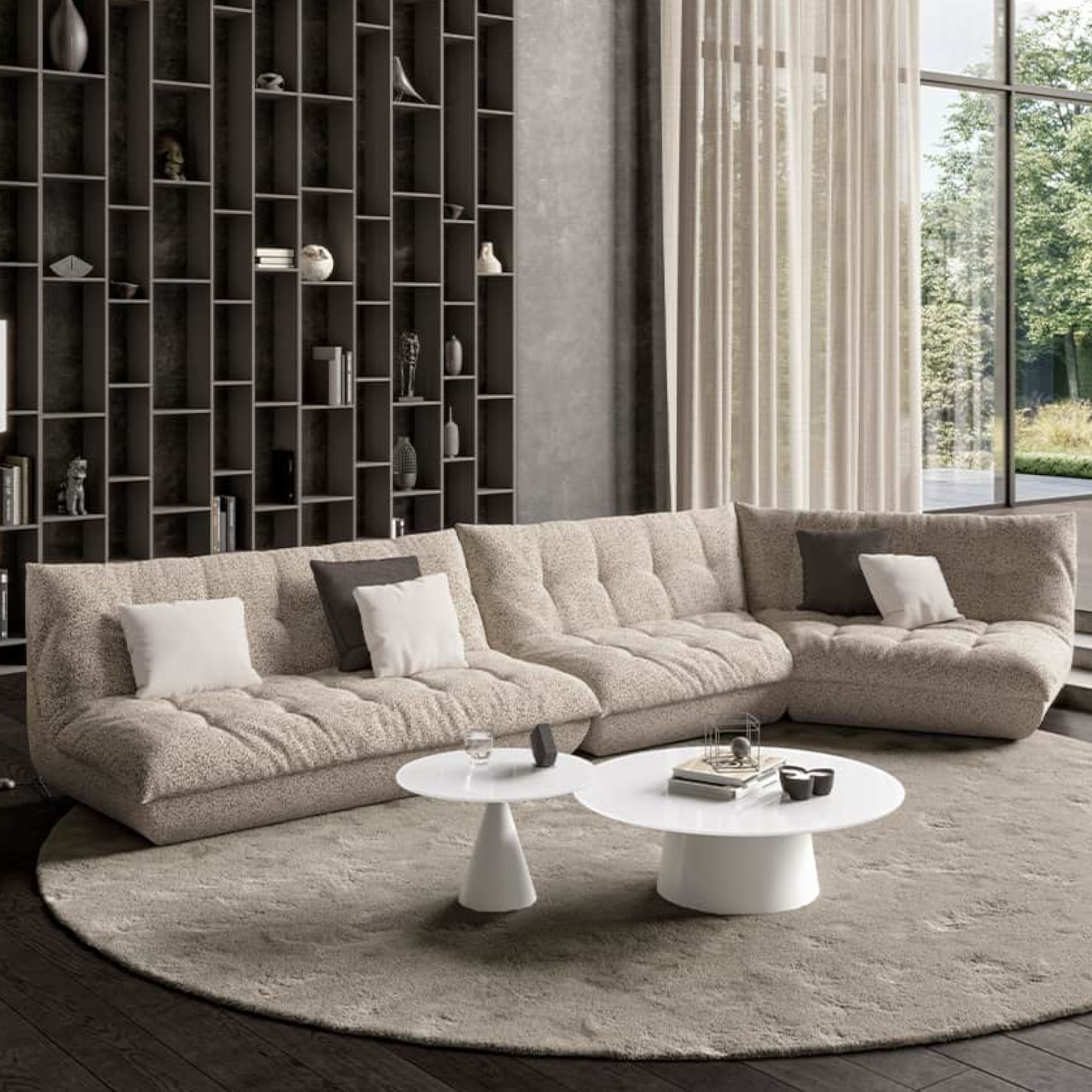 Vor einer hogehn Regalwand steht ein helles Stoffsofa mit gemütlicher Polsterung. Auf dem Boden liegt eine runder Teppich, ergänzt wird die Sitzgruppe durch zwei runde weiße Tische.