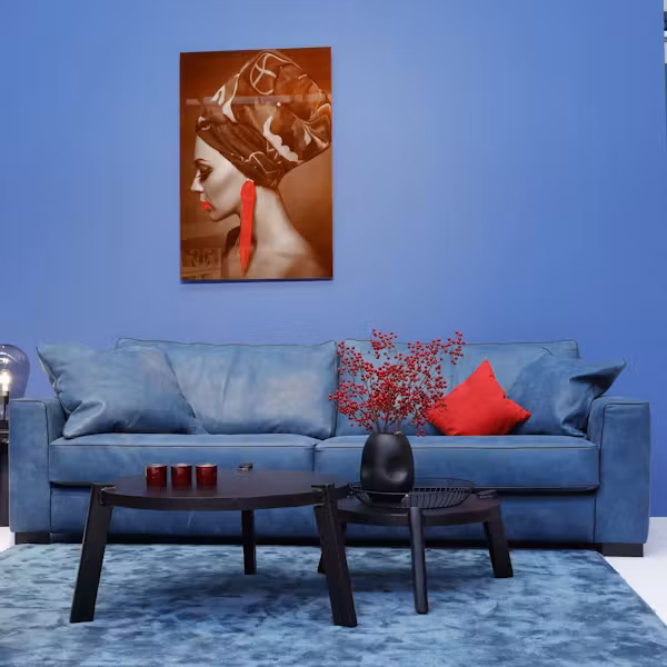 Blaues Sofa vor blauer Wand mit Wandbild und Couchtischen