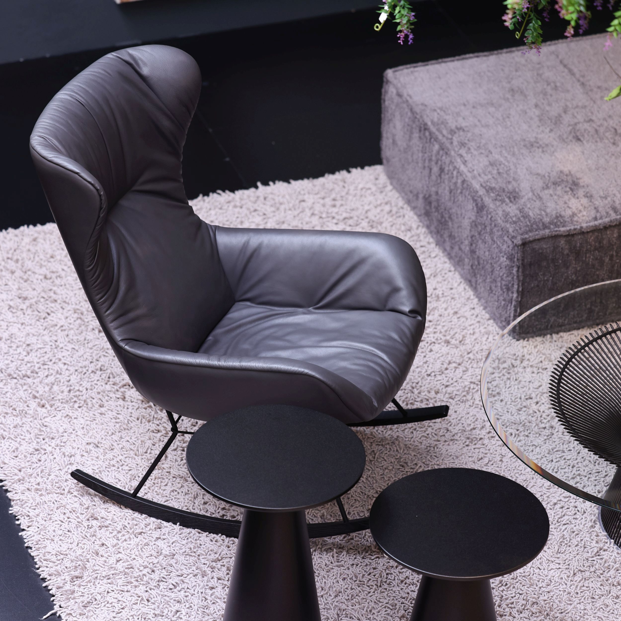 Schaukelstuhl Leya Rocking Wingback Chair von Freifrau  in anthrazitgrauem Leder auf einem hellen Teppich von oben fotografiert.