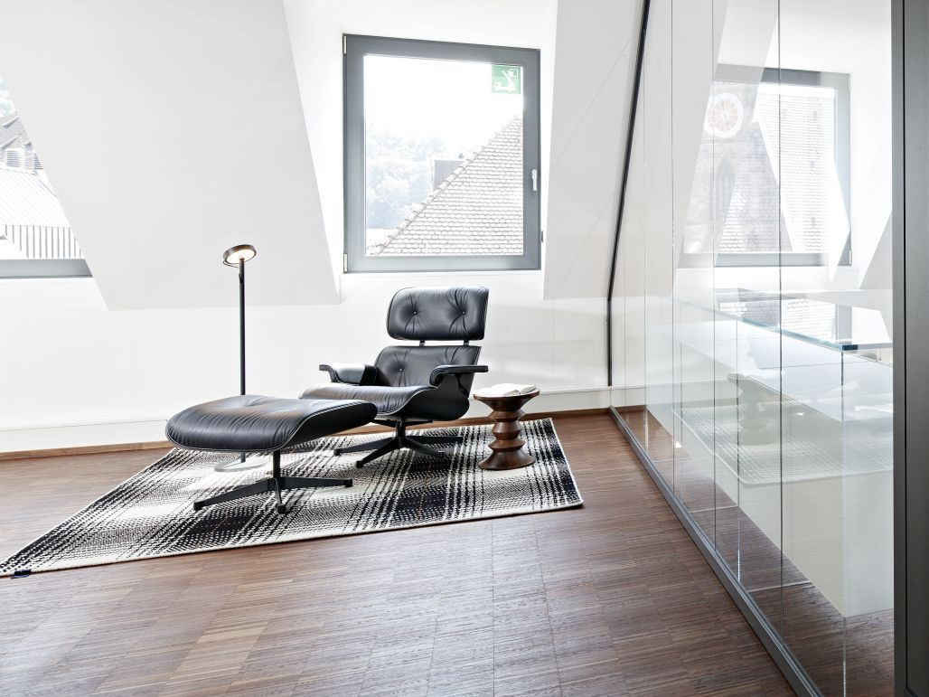 Dachgeschoss mit Eames Lounge Chair auf gemustertem Teppich vor Glaswand
