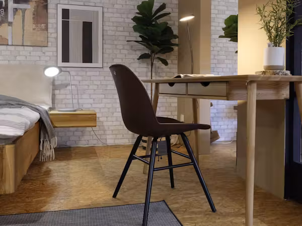 Arbeitsplatz mit Holzschreibtisch und schwarzem Stuhl vor einer Backsteinwand