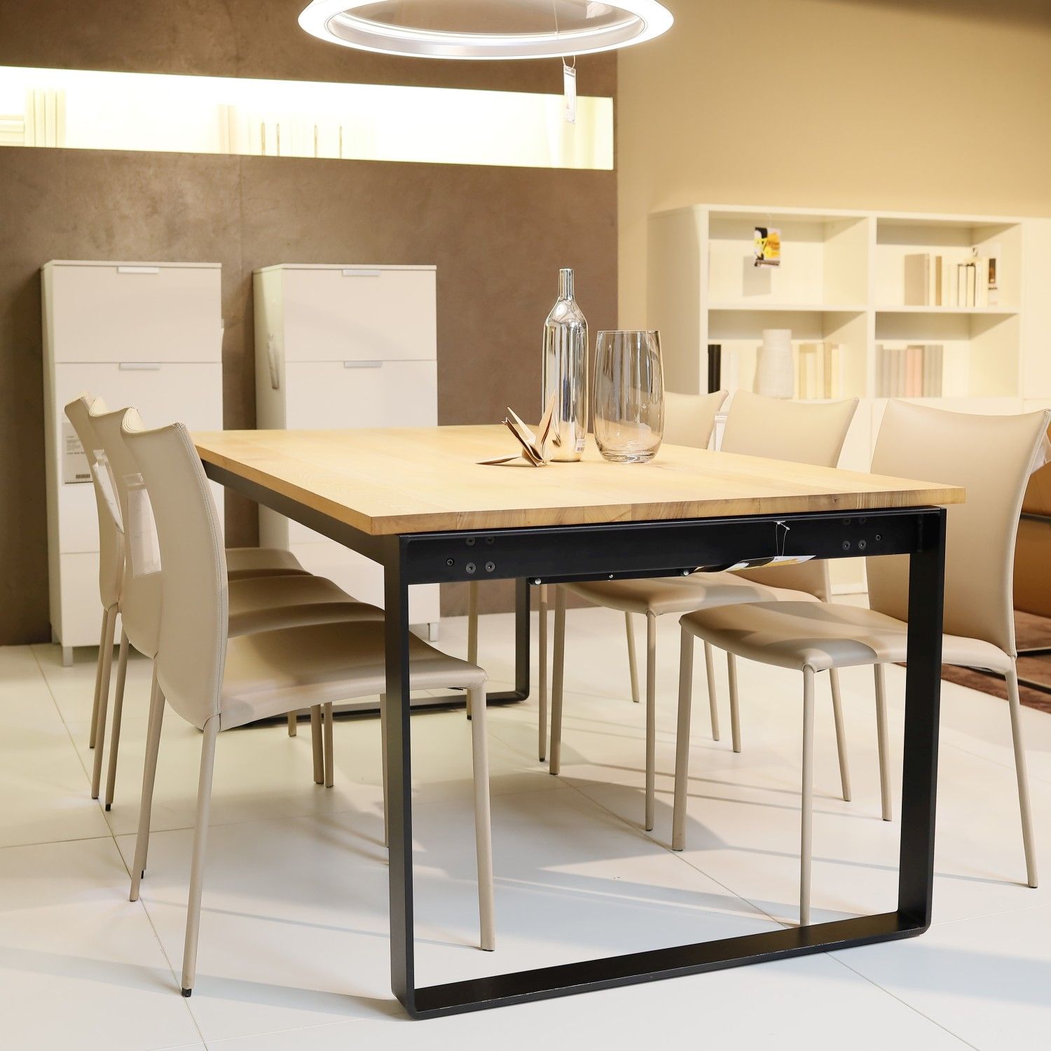 Zu sehen ist der Esstisch Infinity von Riva mit schwarzem Kufen-Unergestell und heller Holzplatte in einem modernen Esszimmer; an dem Tisch stehen sechs beigefarbene Lederstühle.