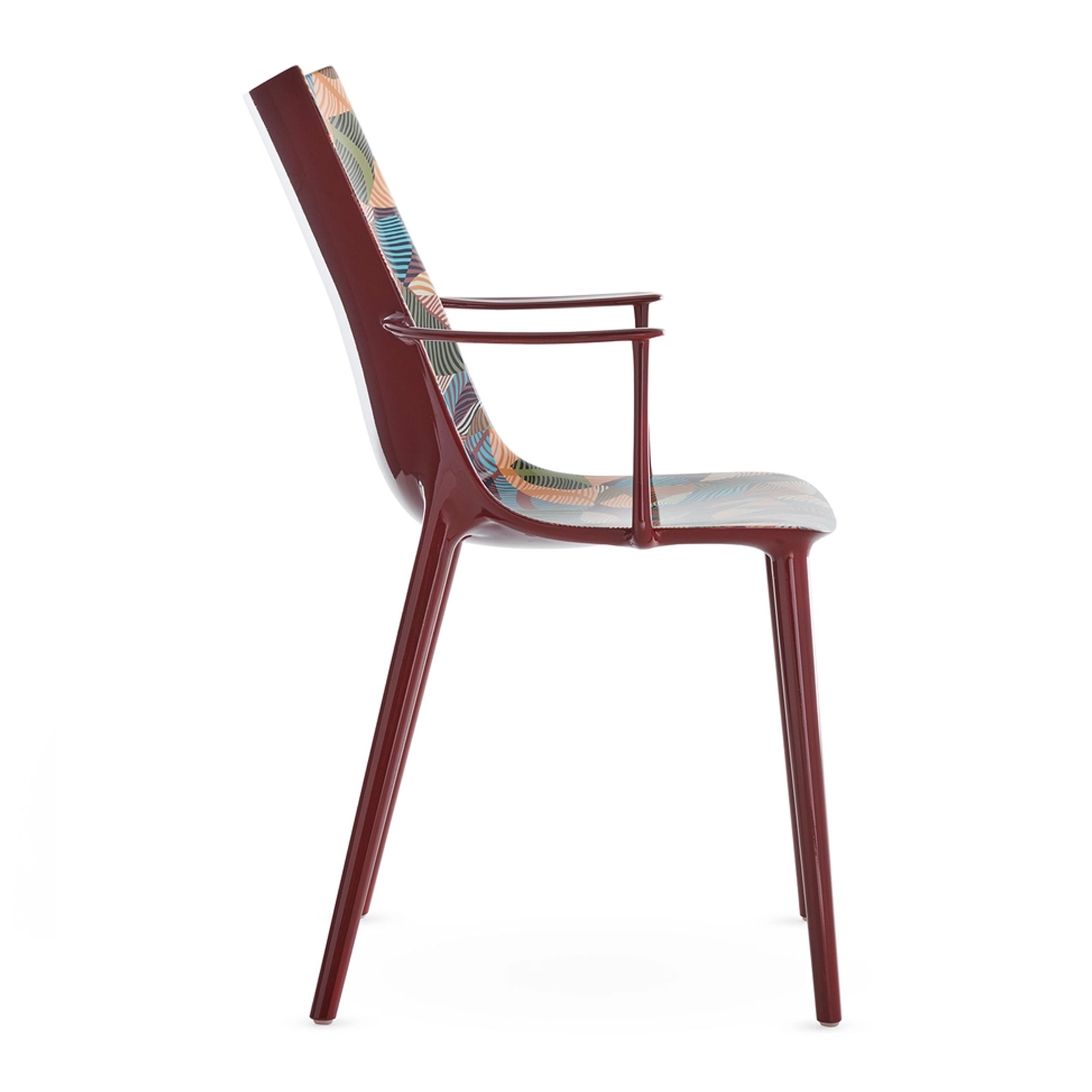 Zu sehen ist in seitlicher Ansicht der Outdoor-Armlehnstuhl H.H.H. aus der Kartell x Liberty-Edition "Graphic Impression" mit bordeauxrotem Gestell und einer mit floralem Muster bedruckten Sitzschale. 