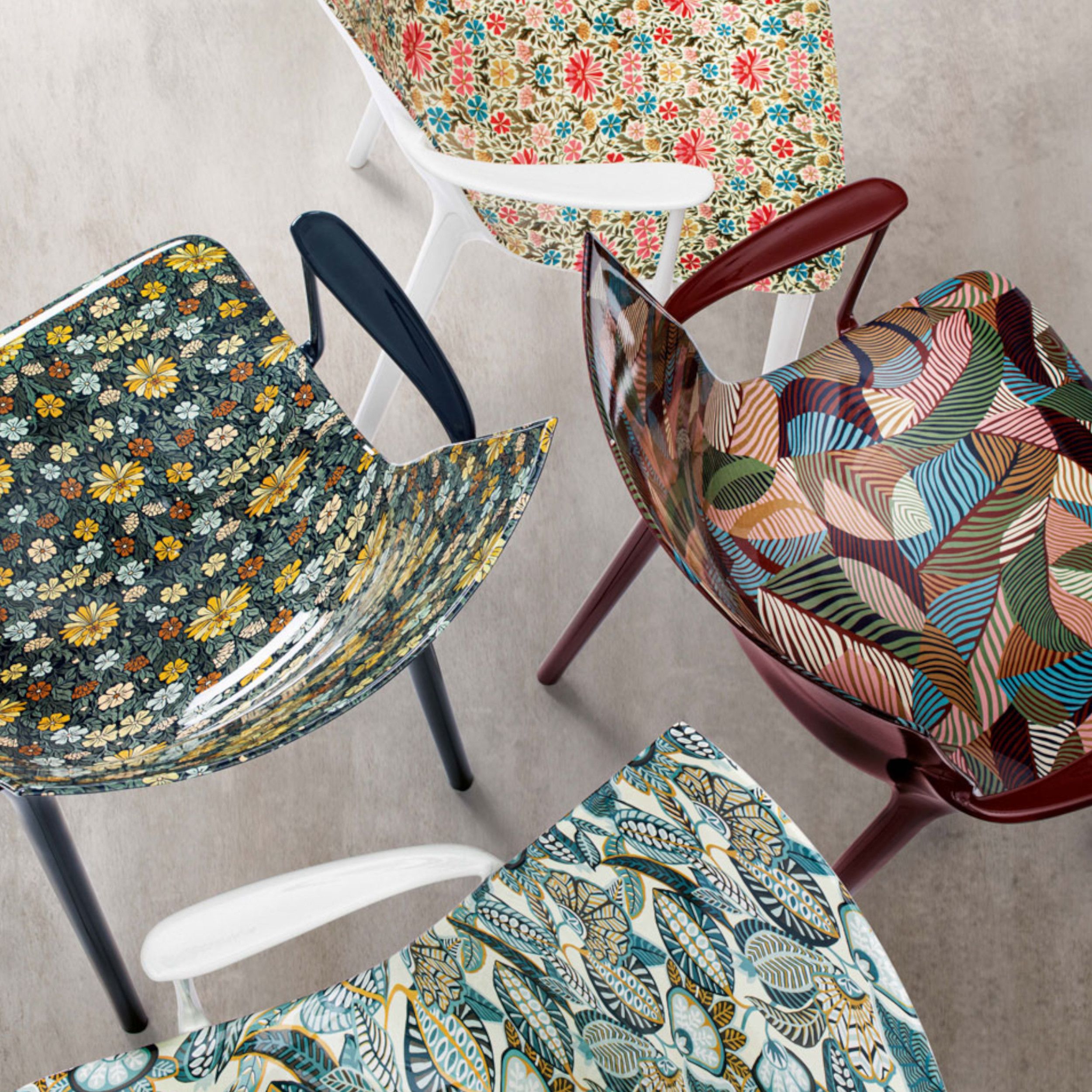 Das Bild zeigt eine Gruppe von vier Armlehnstühlen H.H.H. von Kartell mit unterschiedlich bunt bedruckten Sitzschalen aus der Kartell x Liberty- Edition "Graphic Impression".