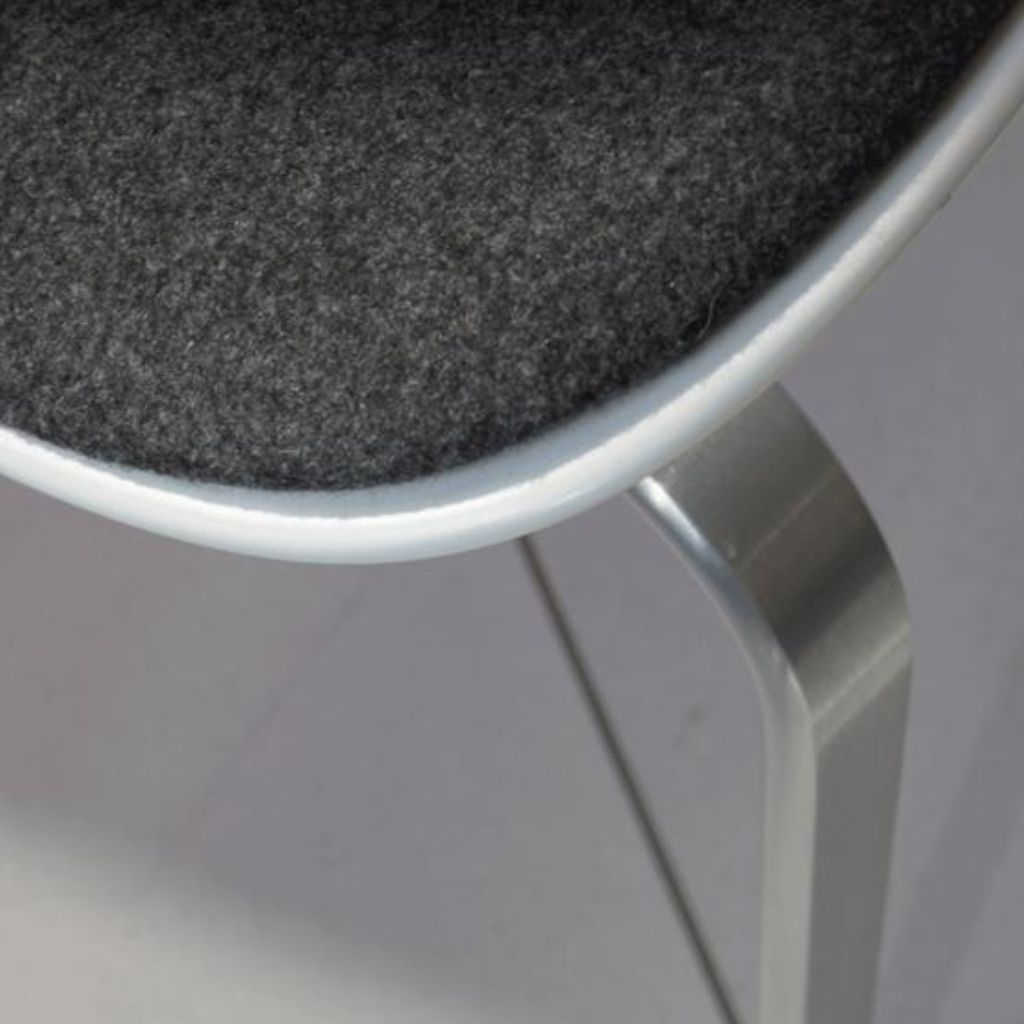 Ein dreibeiniger Stuhl, Modell PK8 von Fritz Hansen, in Detailaufnahme.
Zu sehen ist in Nahaufnahme der Übergang von der weißen Kunststoffschale zur grauen Polsterung; ein Stuhlbein ist ebenfalls zu sehen.
