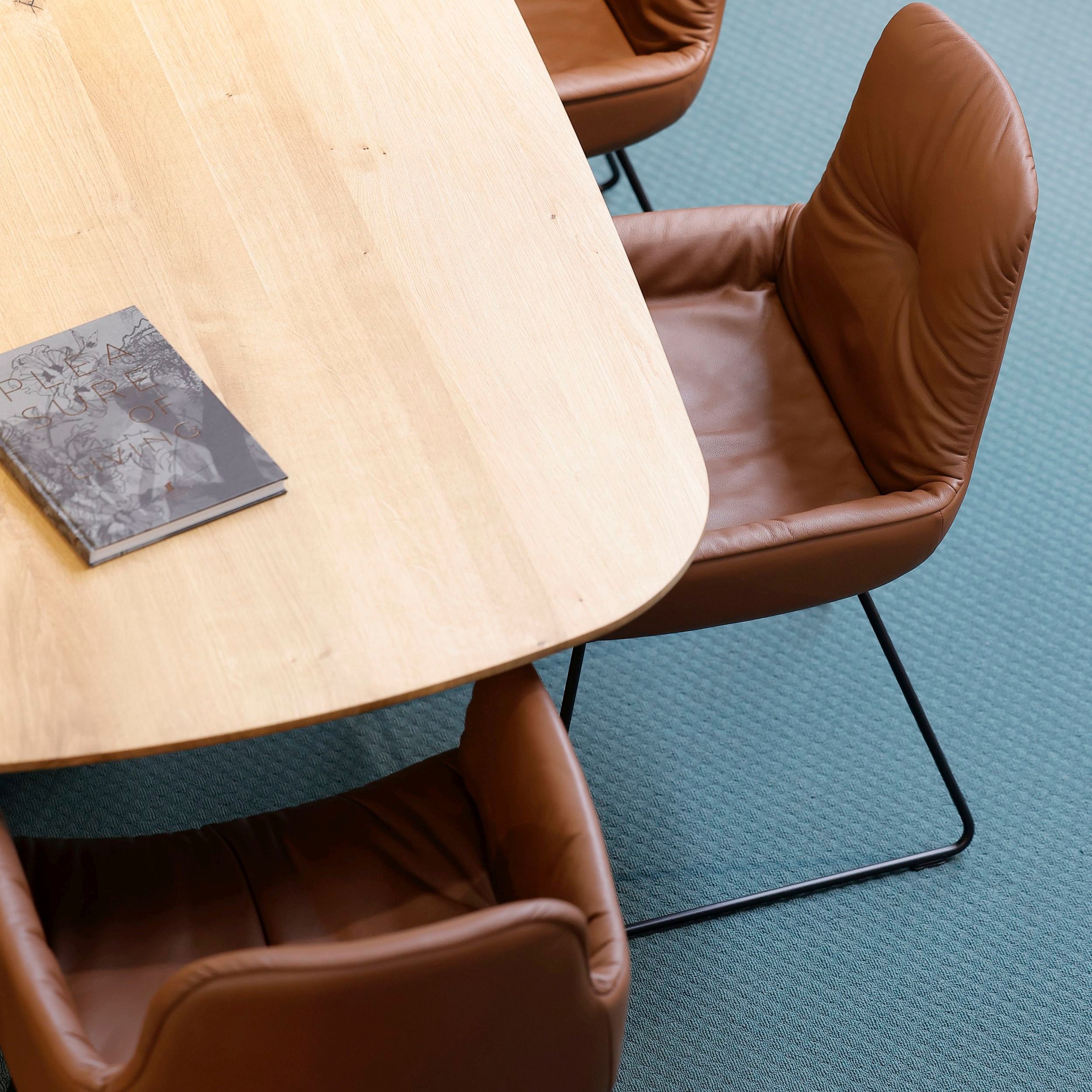 Leya Armchairs von Freifrau in braunem Leder an einem Tisch mit bootsförmiger Holzplatte.