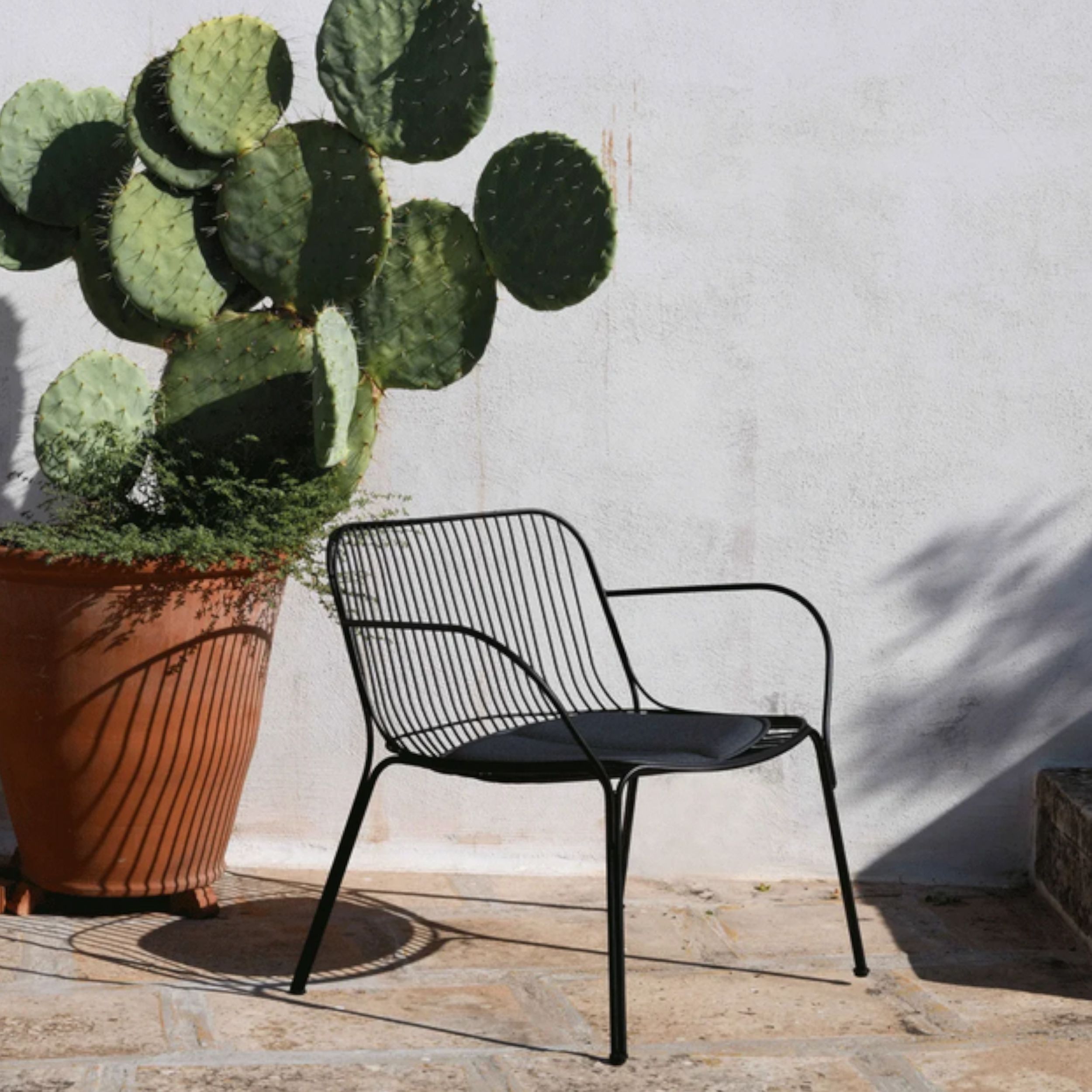 Gartensessel Hiray von Kartell in schwarz mit anthrazitfarbenem Sitzkissen im Milieubild.