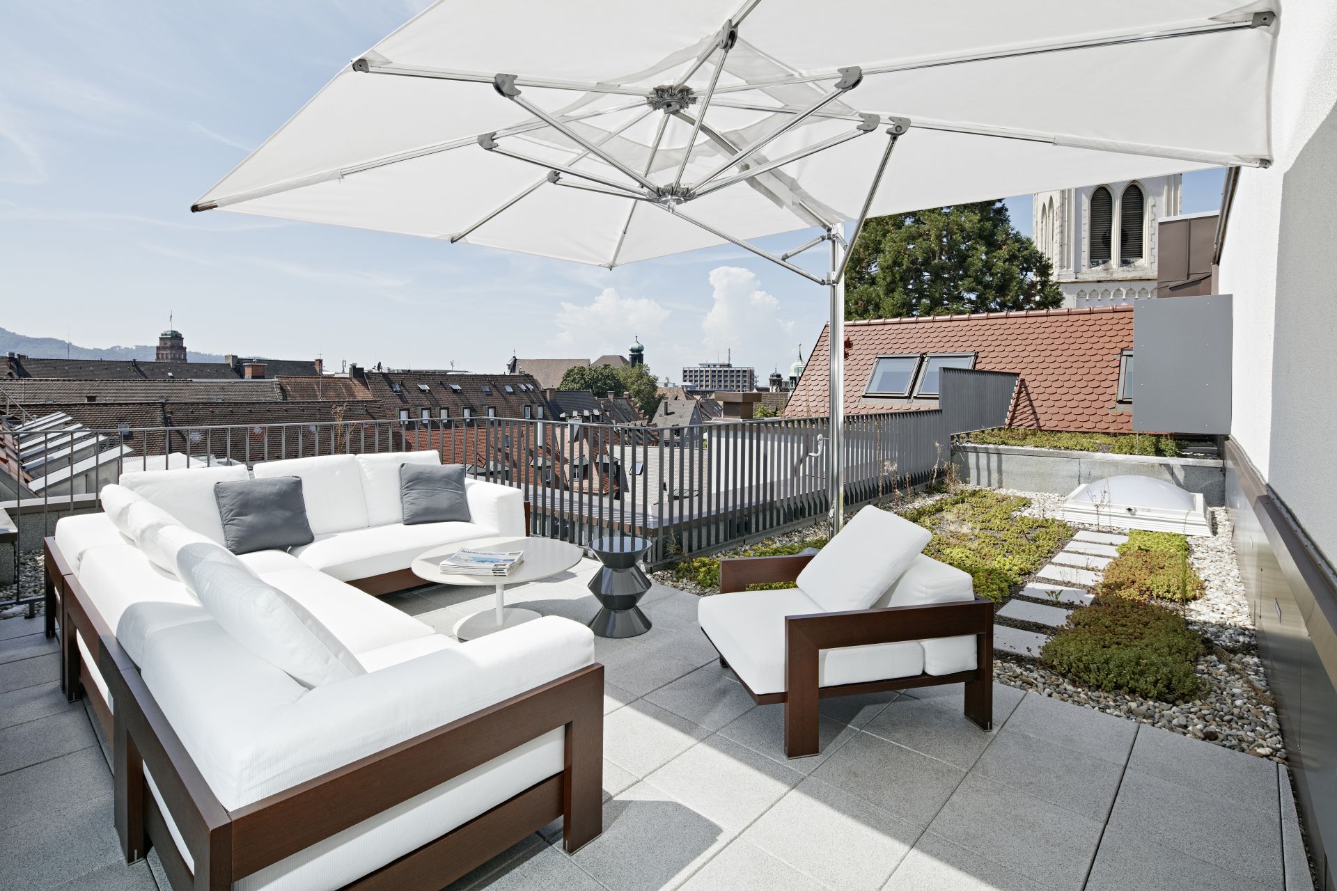 Dachterrasse mit weißen Outdoor-Loungemöbeln und Sonnenschirm