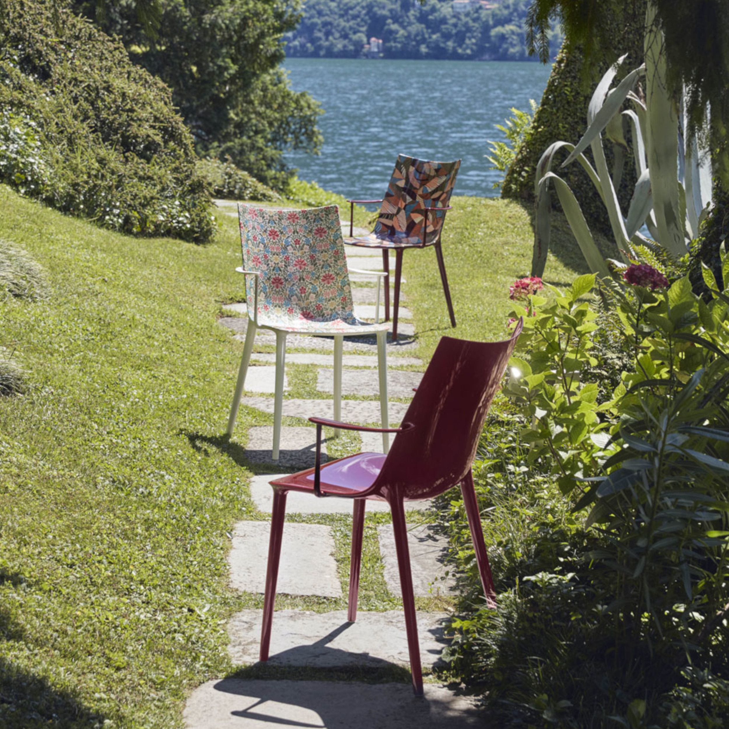 Das Bild zeigt drei Outdoor-Armlehnstühle H.H.H. von Kartell in einem mediterranen Garten mit Blick aufs Wasser.