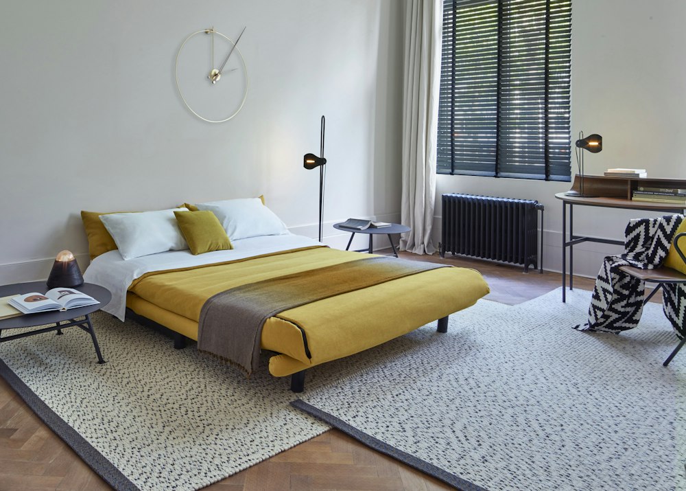 Schlafzimmer mit gelber Tagesdecke, Teppich und Stehleuchte