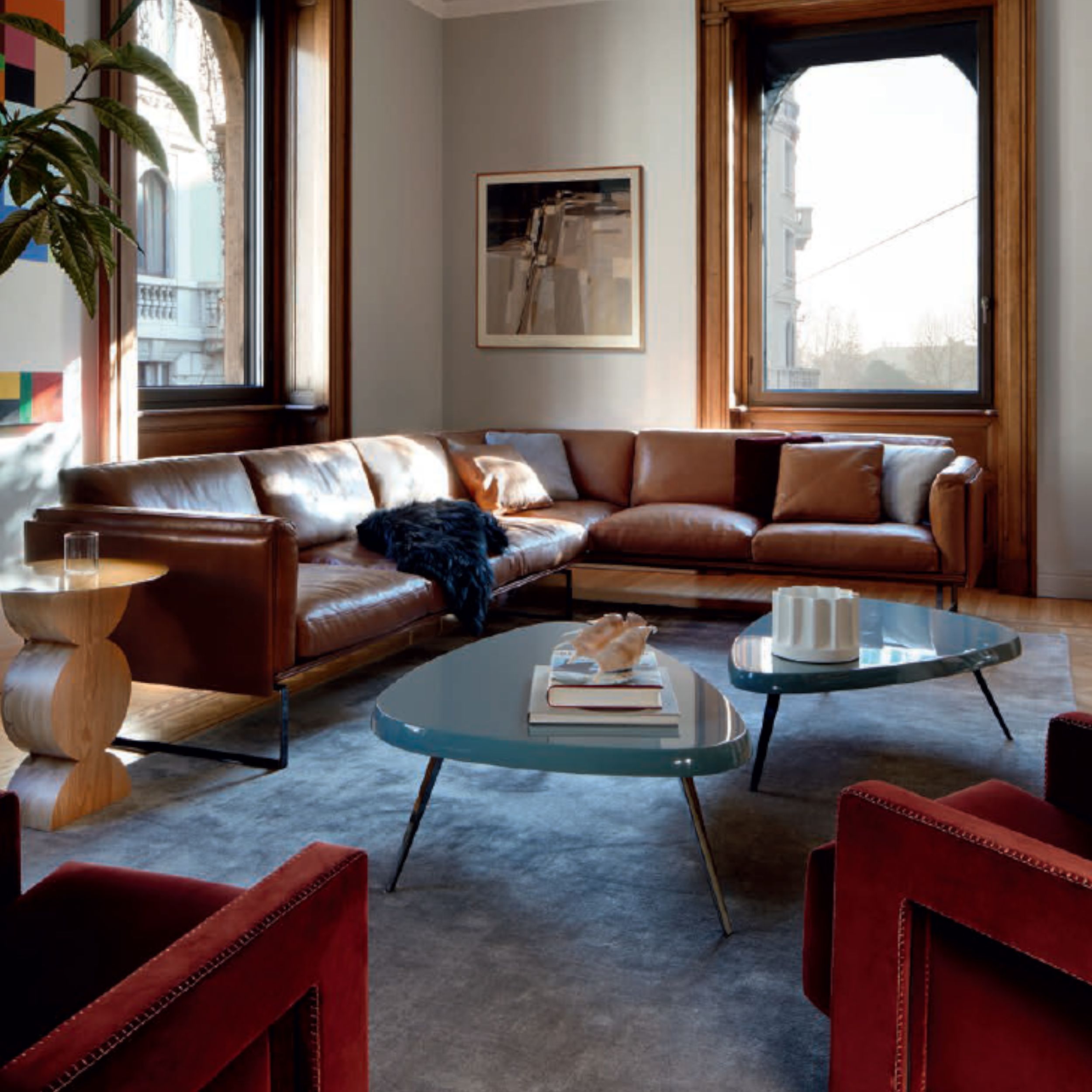 Ein elegantes Wohnzimmer, eingerichtet mit einem braunen Ledersofa kombiniert mit zwei grünen Cocuhtischen und zwei roten Sesseln.
