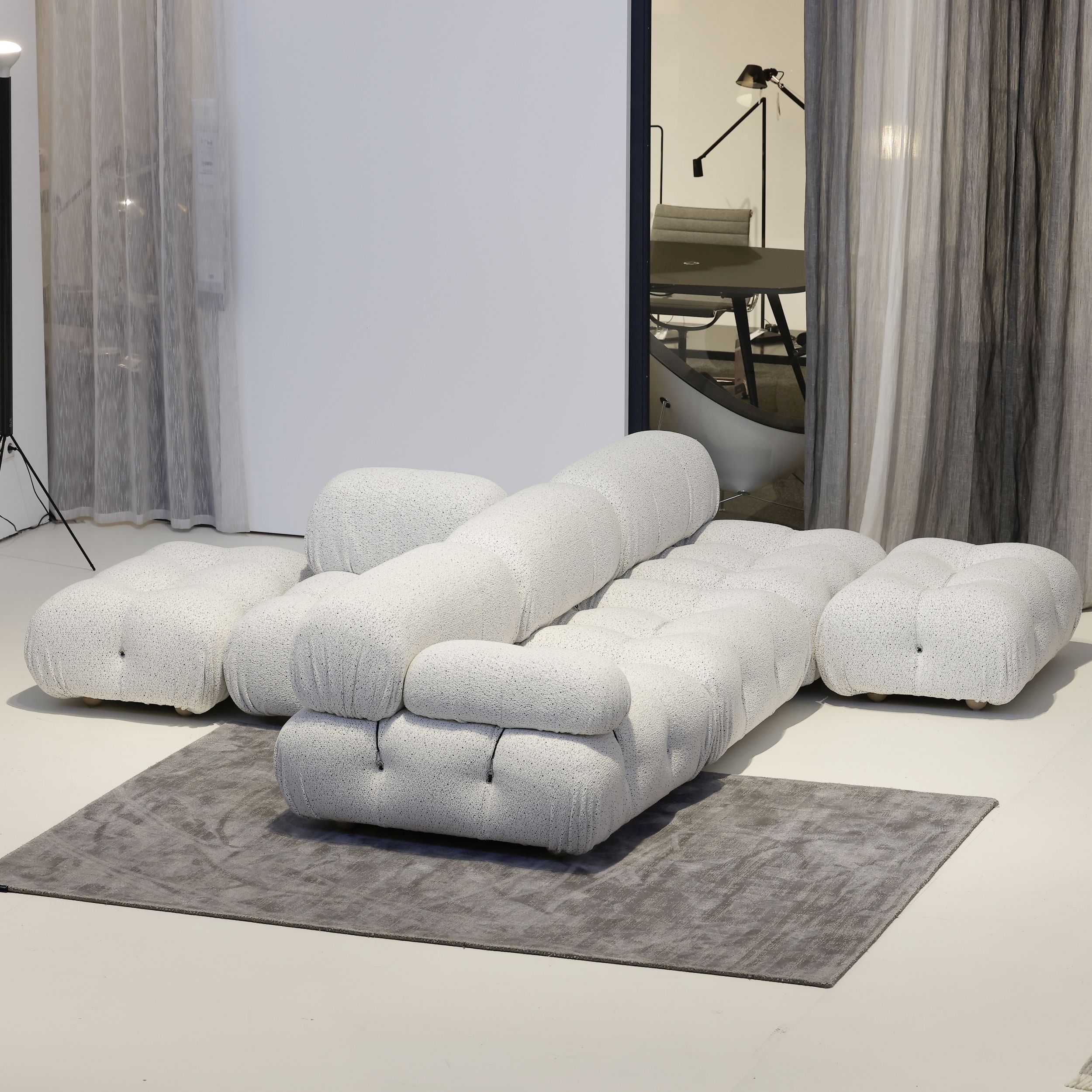 Auf dem Bild sieht man das modulare Sofamodell Camaleonda von B&B Italia in einem modernen Studio. Gezeigt wird das Sofa in einer  Zusammenstellung mit T-förmig Rückenlehnen in der Mitte und Sitzflächen rundherum. Das Sofa ist mit weißem Stoff bezogen.