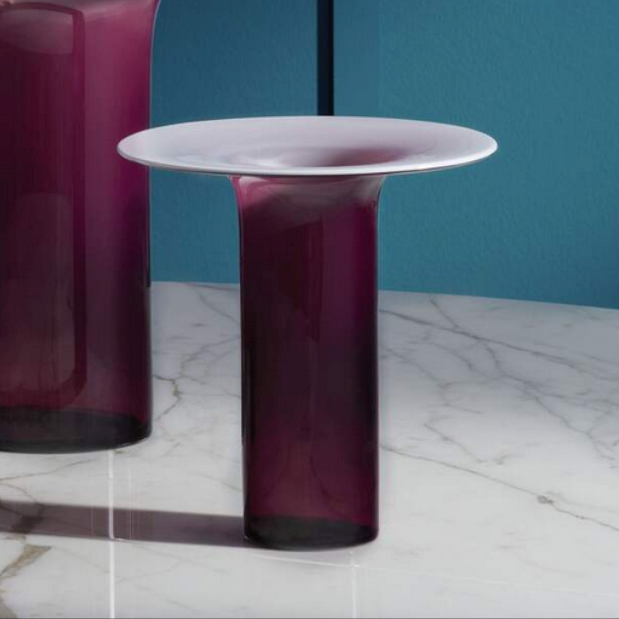 Das Bild zeigt die elegante, amethytfarbene Glasvase Silvan 1 von Cassina auf einer weißen Marmortischplatte.