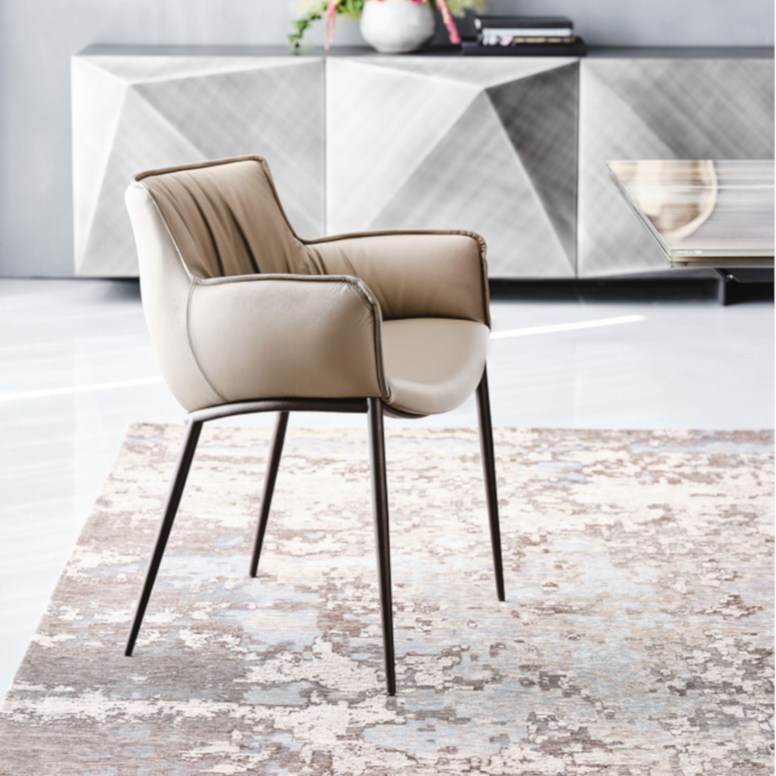 Ein eleganter beigefarbener Lederstuhl, Modell Rhonda von Cattelan Italia, steht auf einem gemusterten Teppich; im Hintergrund sieht man ein graues Sideboard.