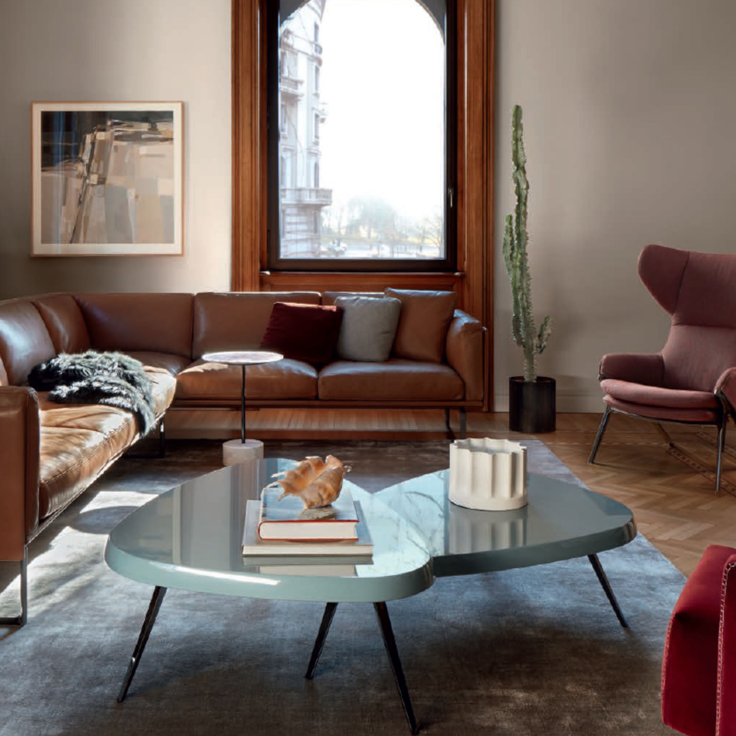 Ein elegantes Wohnzimmer mit einem braunen Ledersofa , einem modernen Ohrensessel und zwei dreibeingen, grünen Couchtischen im Vordergrund.