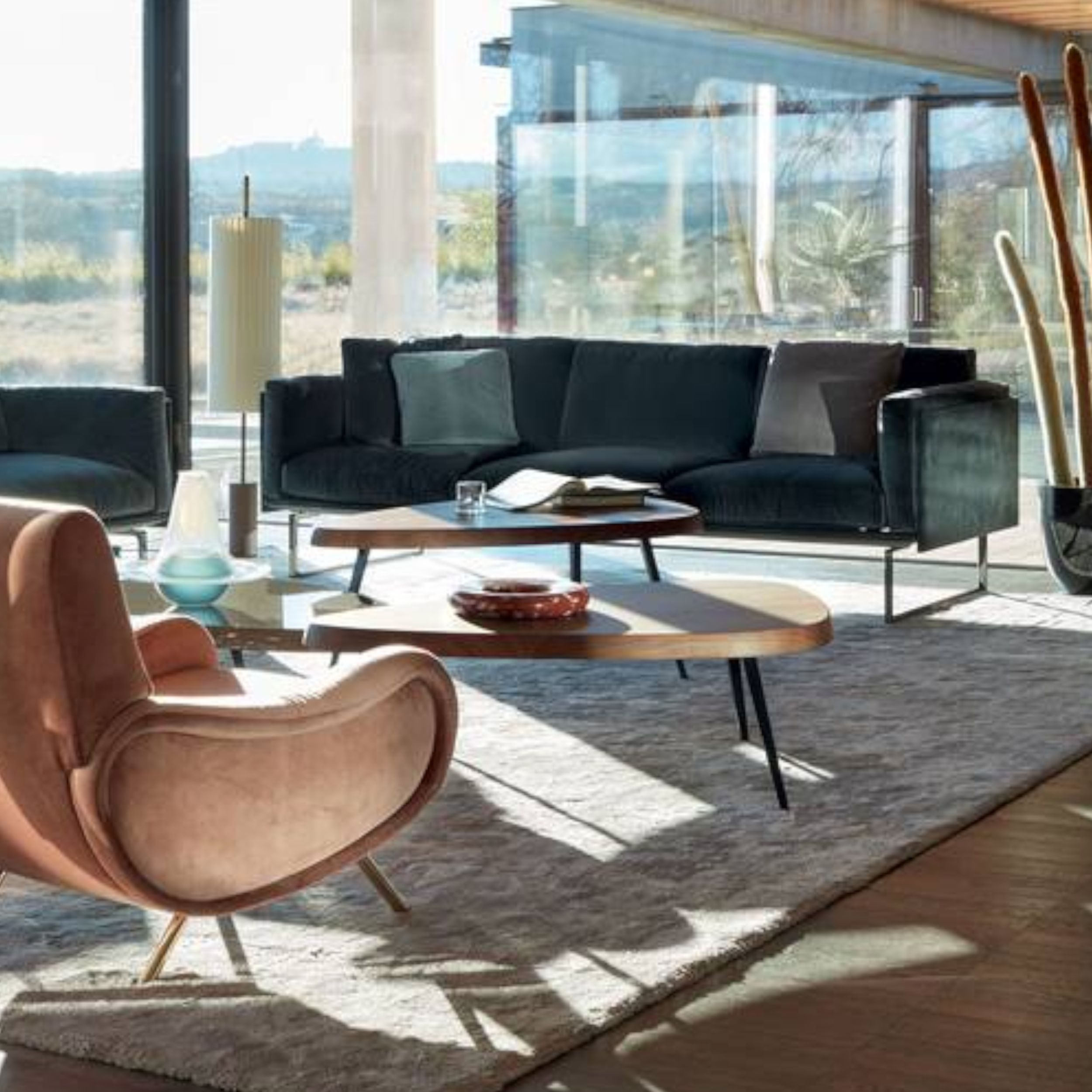 Helles, modernes Wohnzimmer, ausgestattet mit petrolfarbenen Stoffsofas, einem rosafarbenen Sessel und mehreren Cassina-Couchtischen auf einem flauschigen Teppich.