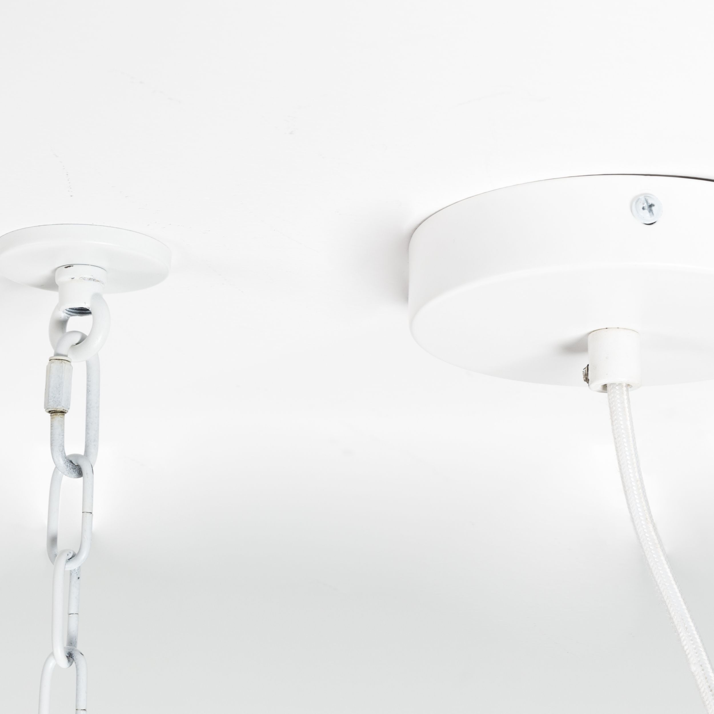 Nahaufnahme der Deckenbefestigung einer weißen Röhrenlampe mit rundem Baldachin, weißem Stoffkabel und separater Kettenaufhängung.
