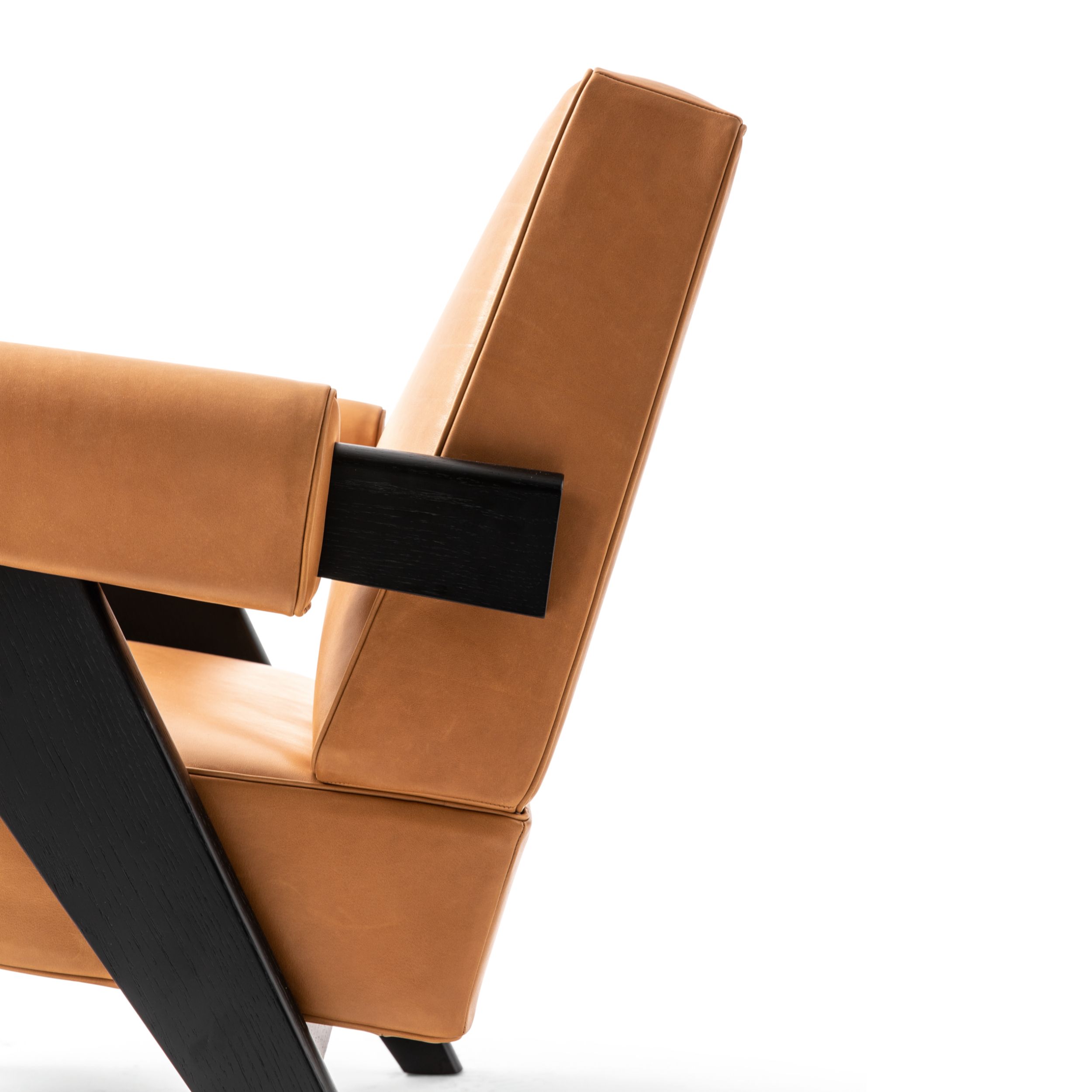 Das Bild zeigt in einer seitlichen Detailaufnahme den Sessel Capitol Complex Armchair von Cassina vor einem weißen Hintergrund. Das Holzgestell des Sessels ist schwarz, die Lederpolster sind braun.