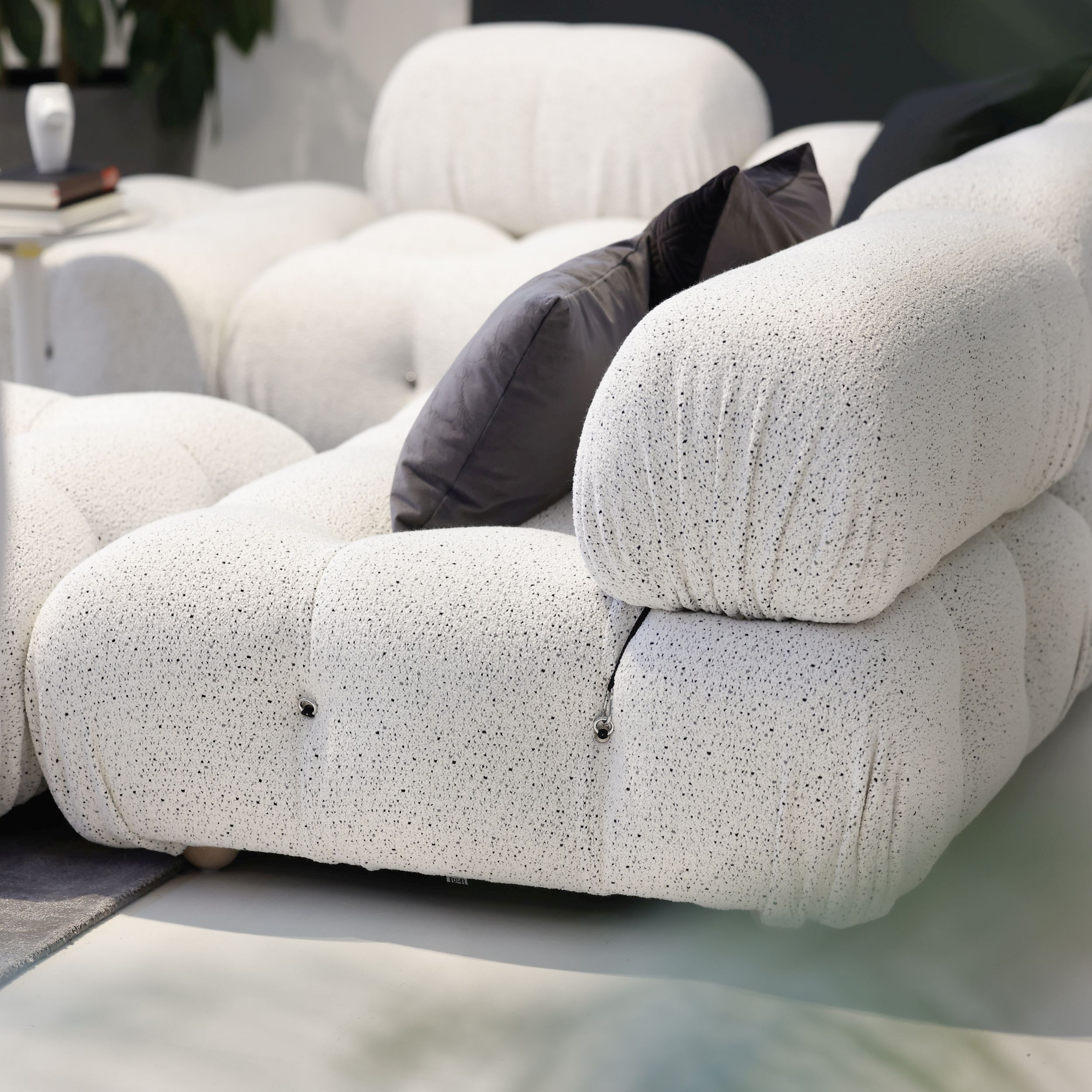 Auf dem Bild sieht man das modulare Sofamodell Camaleonda von B&B Italia in einer Nahaufnahme von der Seite. Der Bezugsstof ist weiß mit dunklen Pünktchen, auf dem Sofa liegen dunkelgraue Kissen.