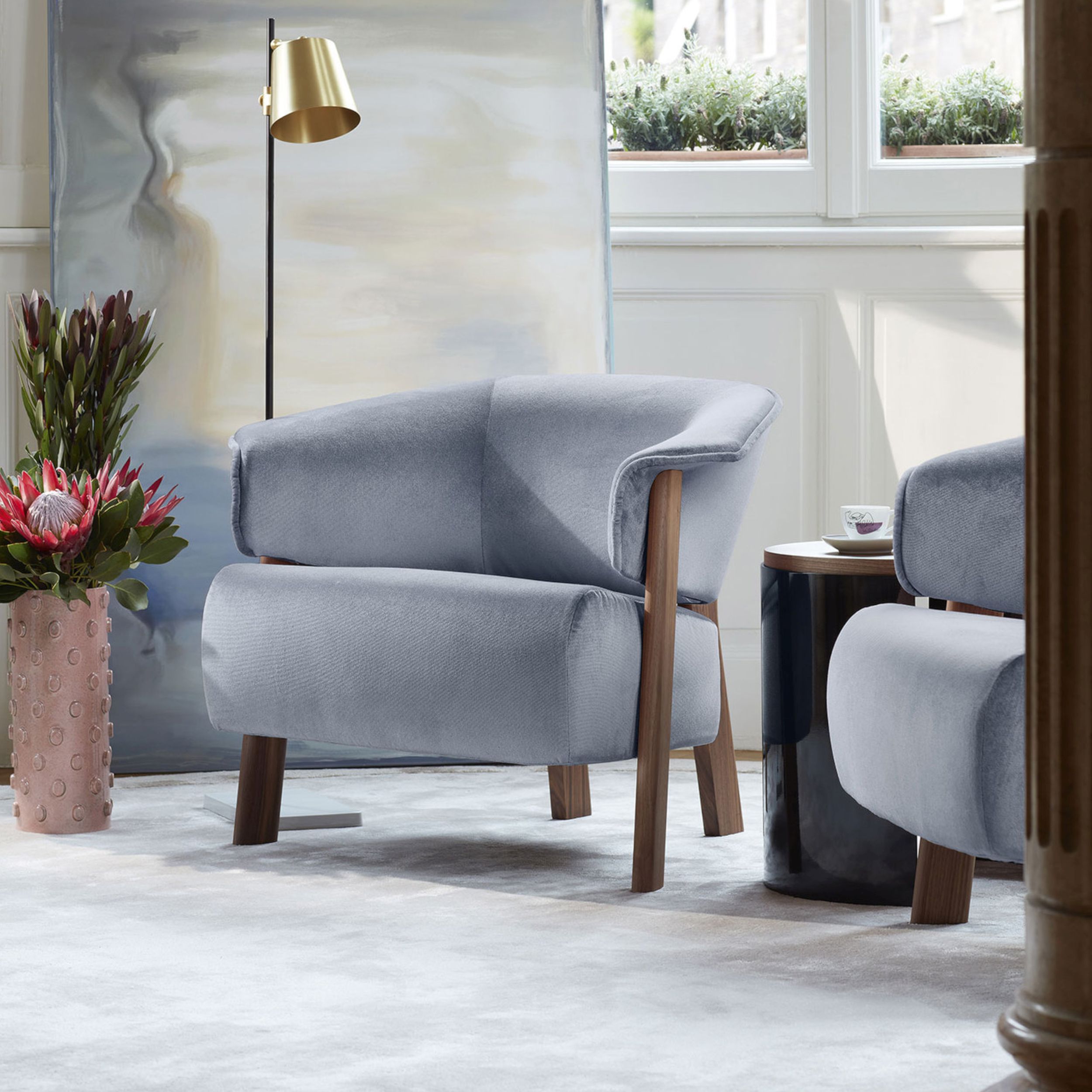 Eleganter, hellblau gepolsterter Sessel "Back Wing Armchair" von Cassina steht neben einer mattgoldenen Leseleuchte auf einem hellen Teppich.