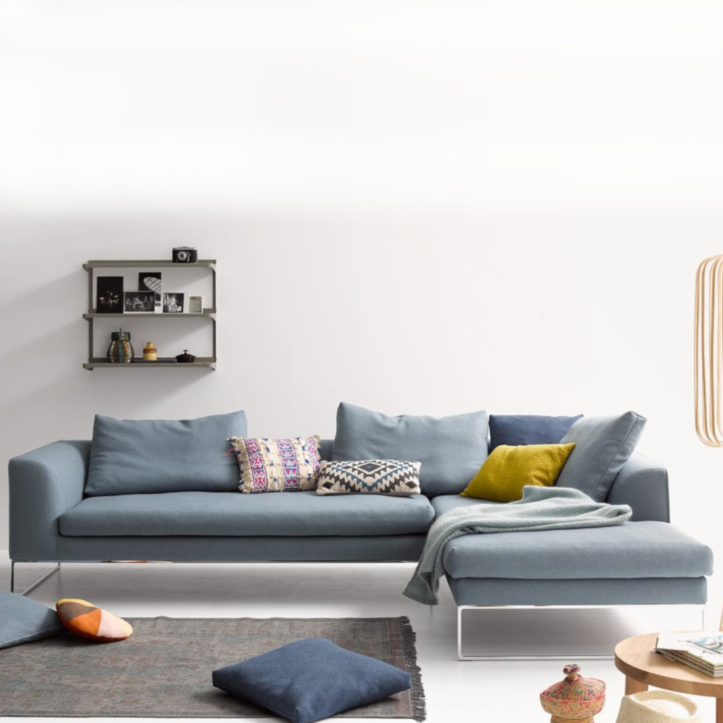 Modernes Wohnzimmer mit einem blauen Sofa Mell Lounge von Cor und ergänzt durch bunte Kissen und einen grauen Teppich.