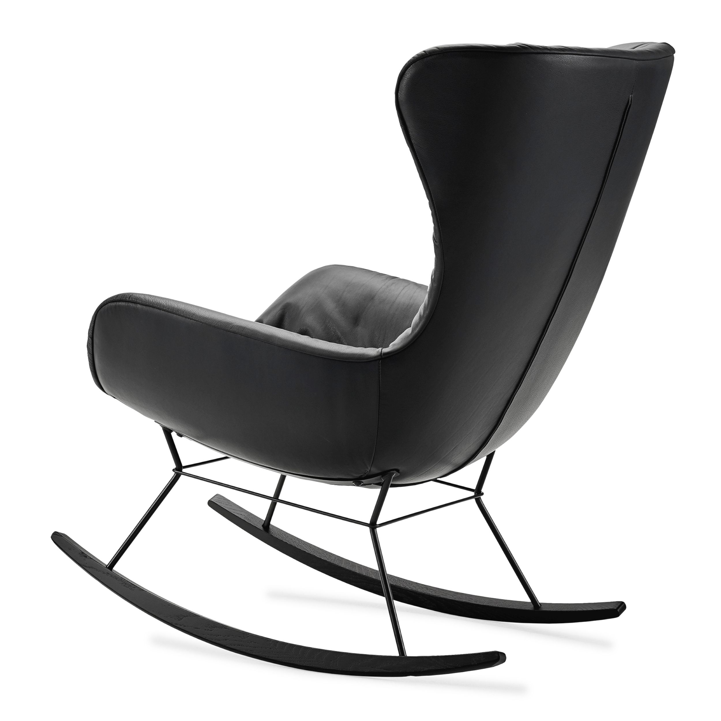 Ein Schaukelstuhl in anthrazitgrauem Leder, Modell Leya Rocking Wingback Chair von Freifrau, in Ansicht von schräg hinten vor einem weißen Hintergrund.