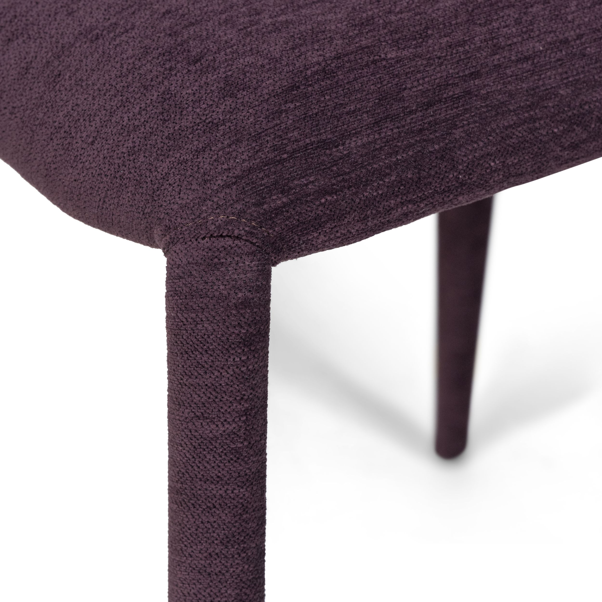 Zu sehen ist in einer Detailaufnahme die Verbindungsstelle zwischen Sitzfläche und Stuhlbein des Stuhlmodells Assisi von Willisau. Der ganze Stühl inklusive der Bene ist mit violettem Stof bezogen.